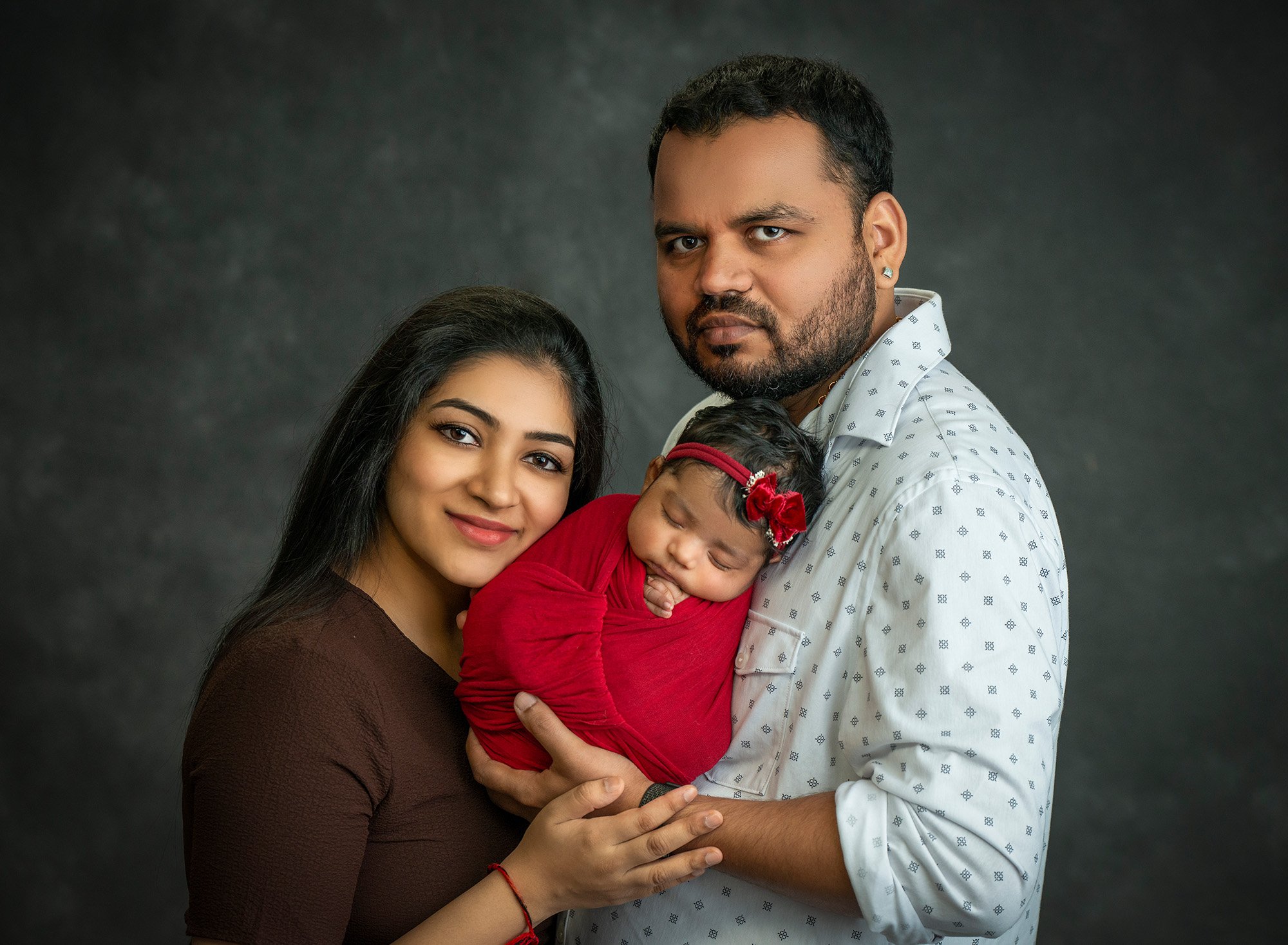 new parents posing with newborn baby girl swaddled in red