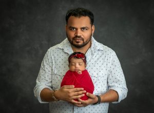 new dad cradling newborn baby girl swaddled in red
