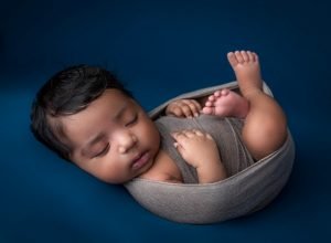 newborn baby girl asleep tucked in grey swaddle on blue background
