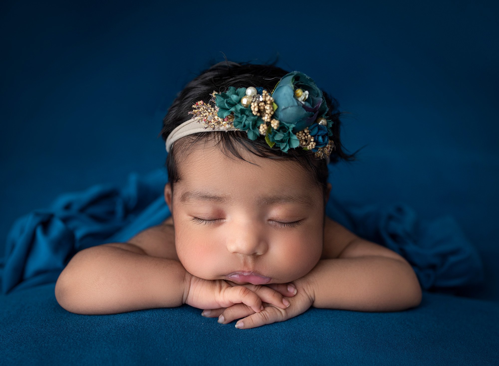 newborn baby girl asleep in blue blankets wearing blue floral headband