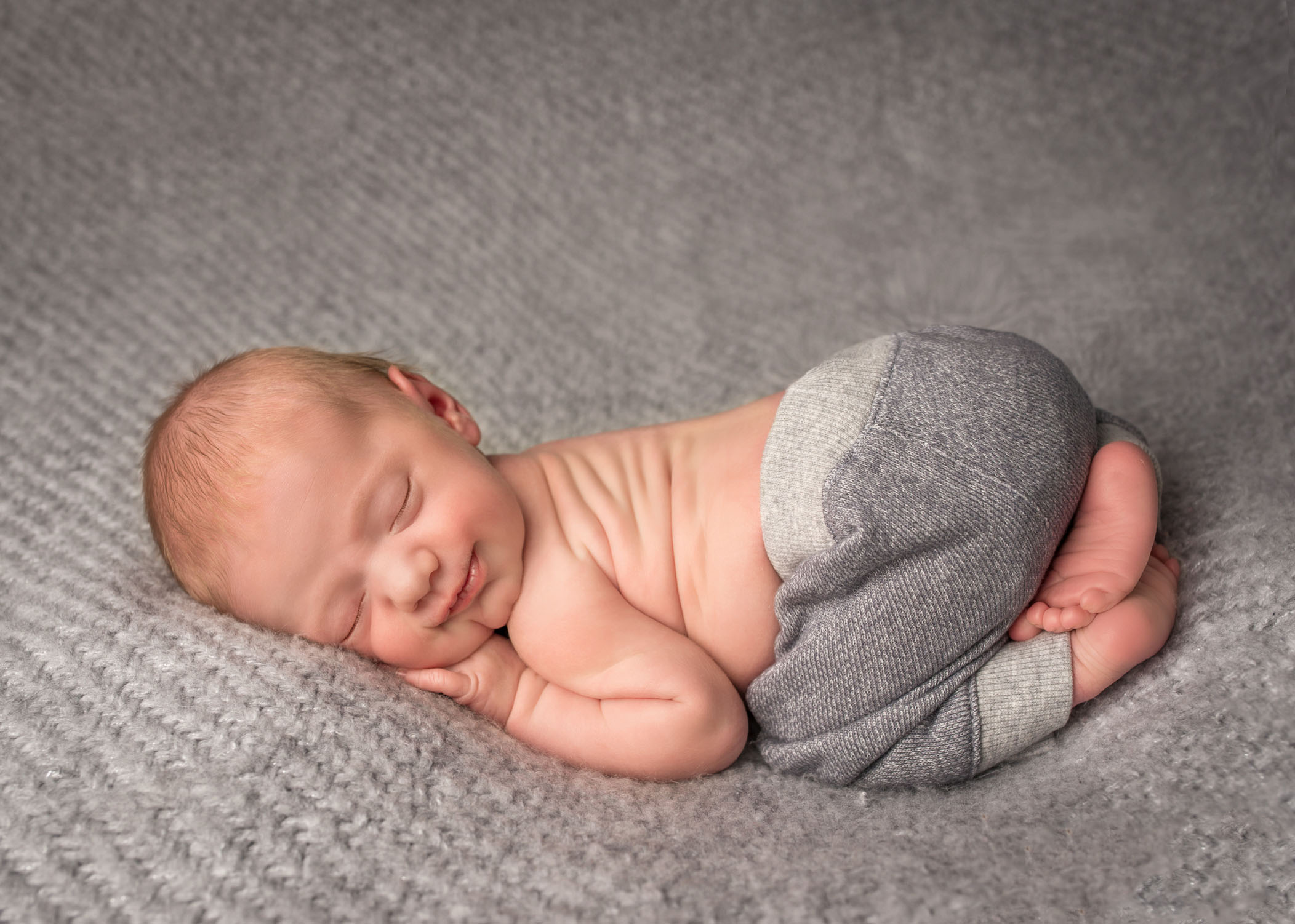smiling newborn baby sleeping in bum up pose on grey blanket