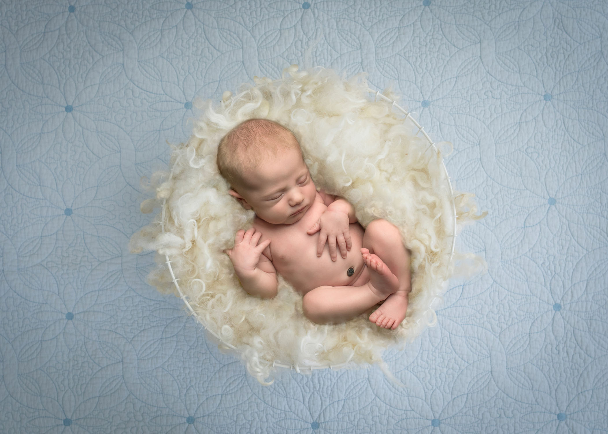 Newborn baby boy sleeping in cream fluff basket on blue background