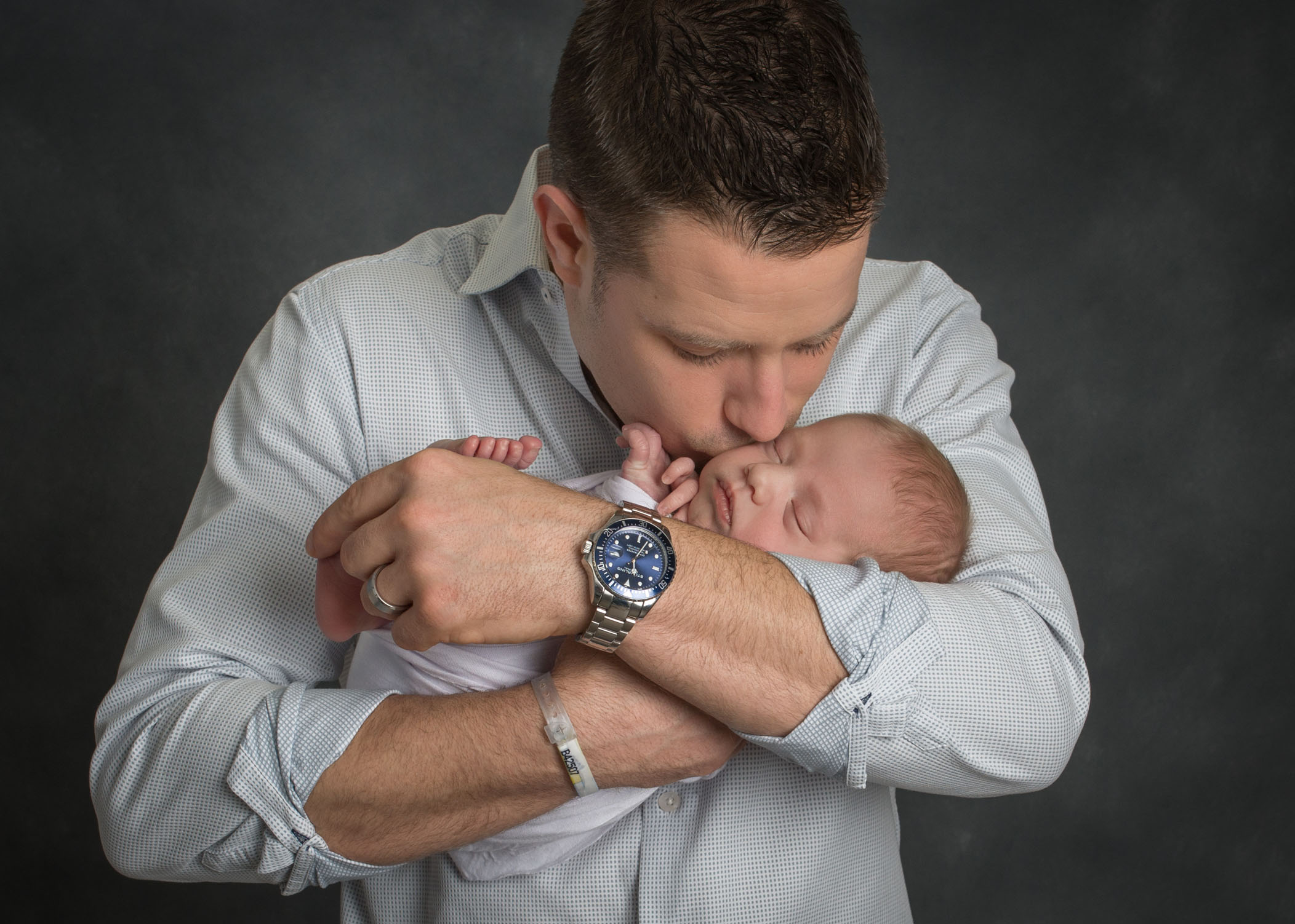 New Dad holding and kissing newborn son in his arms