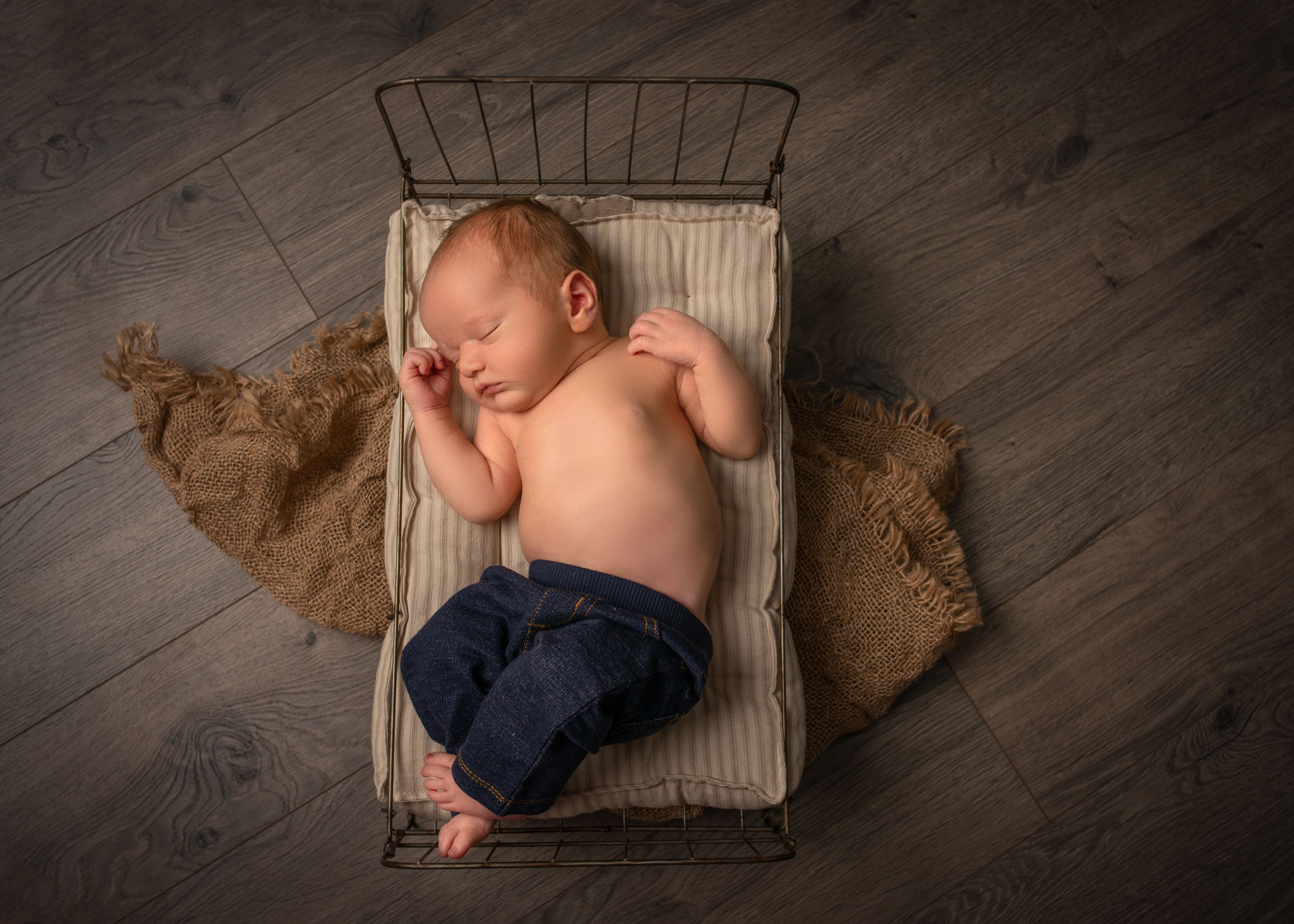 Newborn baby boy sleeping on old fashioned cot wearing jeans