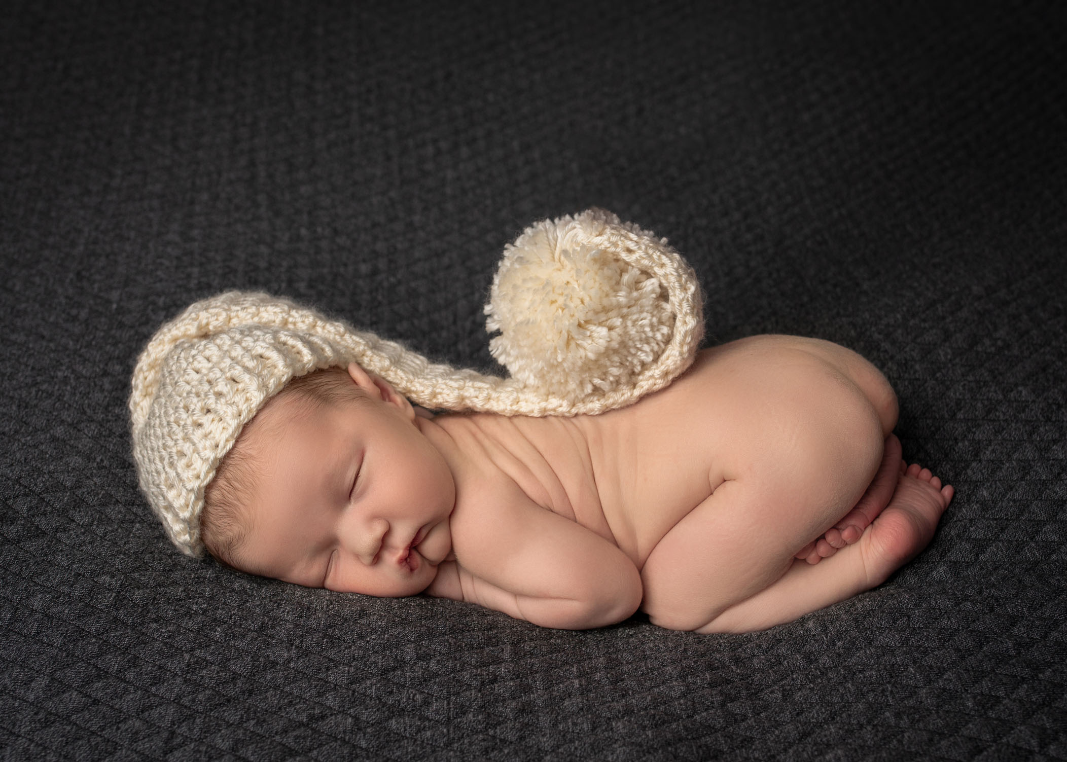 Newborn sleeping in bum up pose with long knitted hat on his head