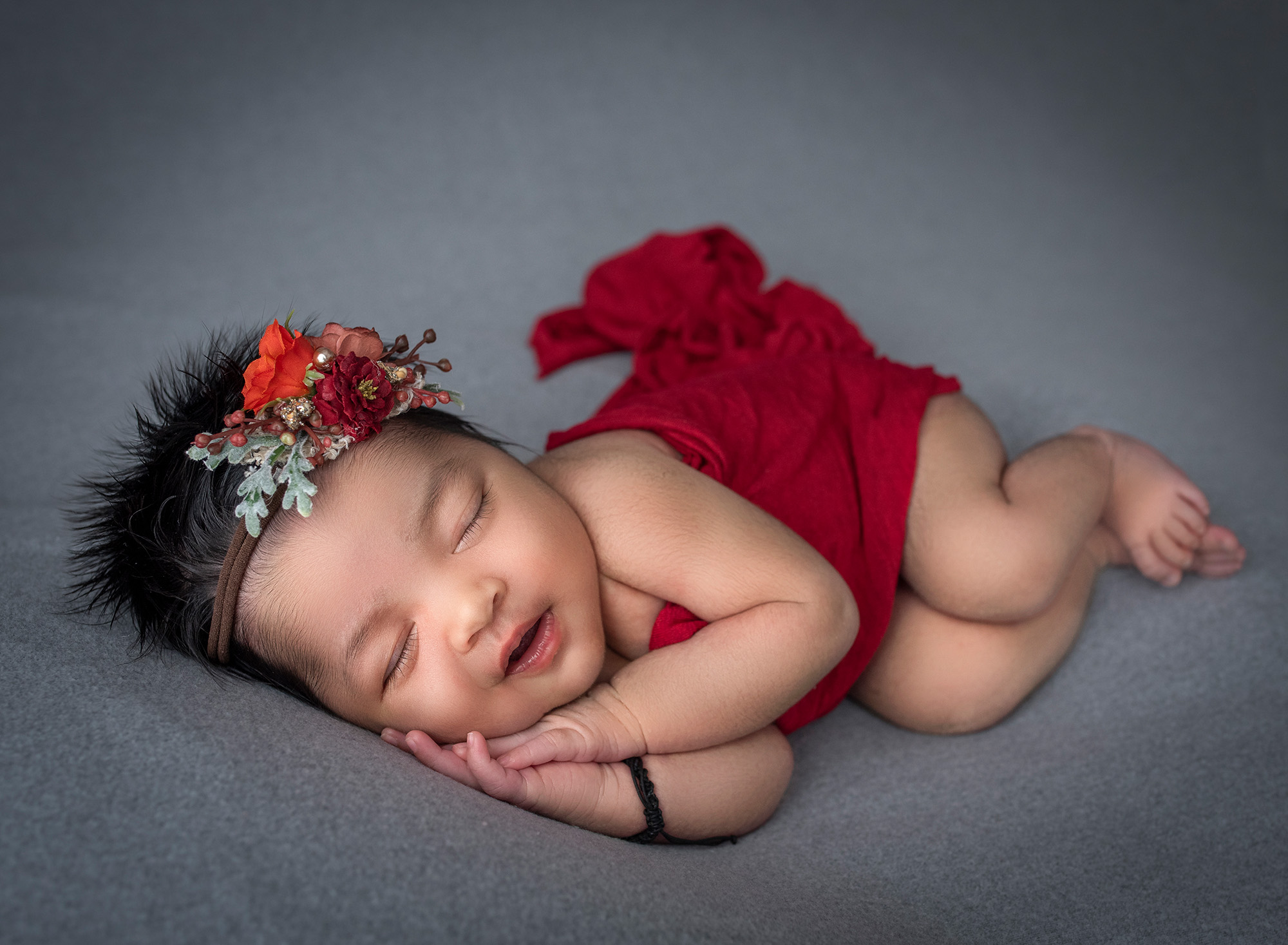 newborn baby girl asleep on her side happily smiling draped in red