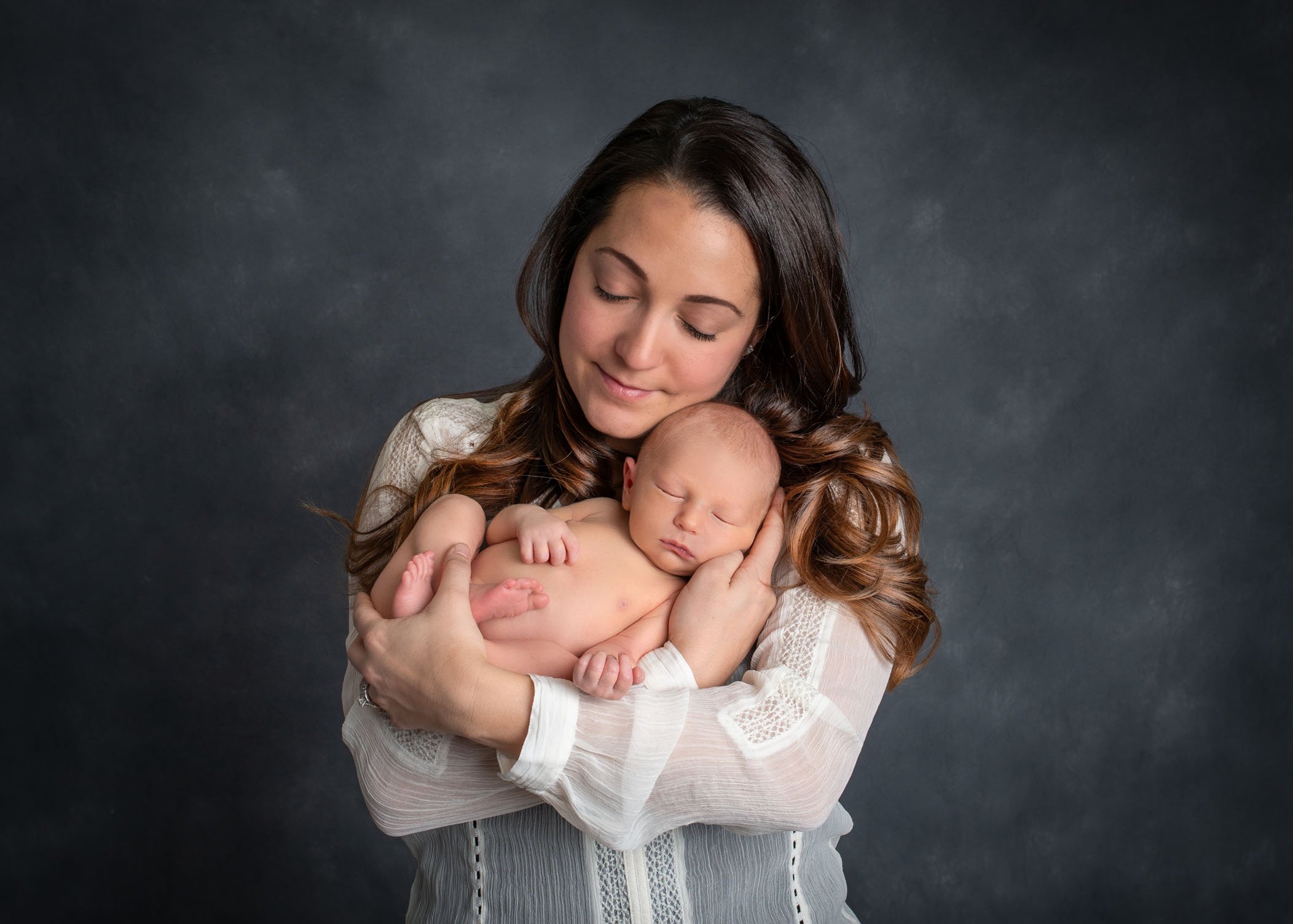 Mom holding newborn son in her arms with eyes closed