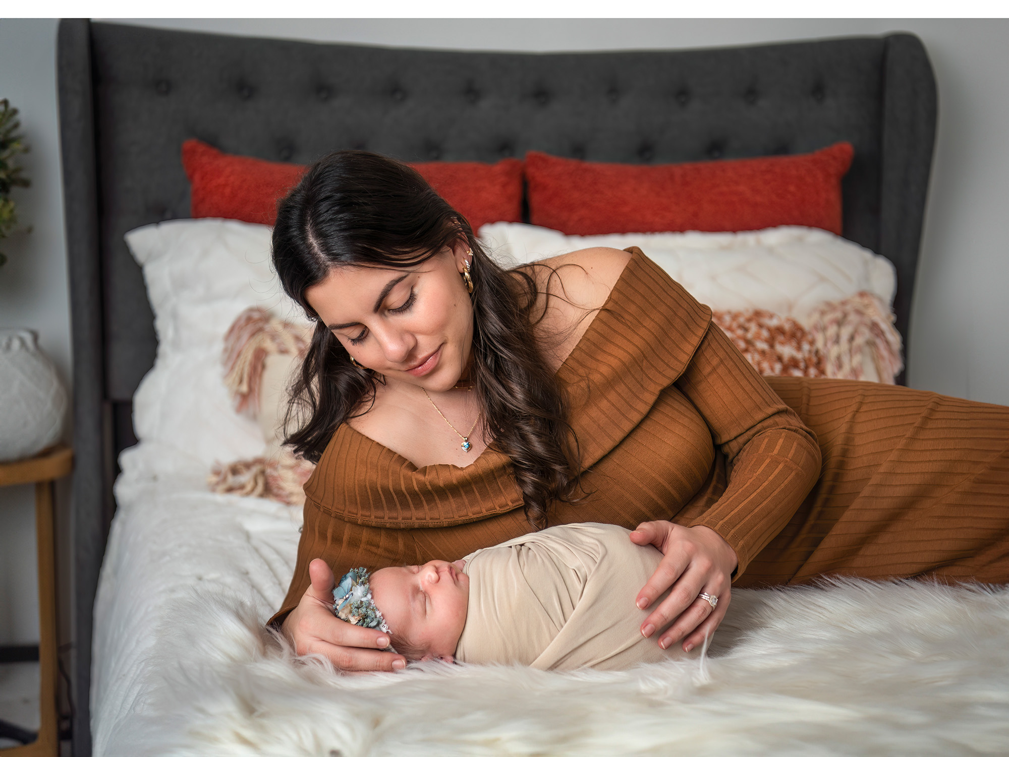 Brunette mom laying on bed looking down at newborn baby girl