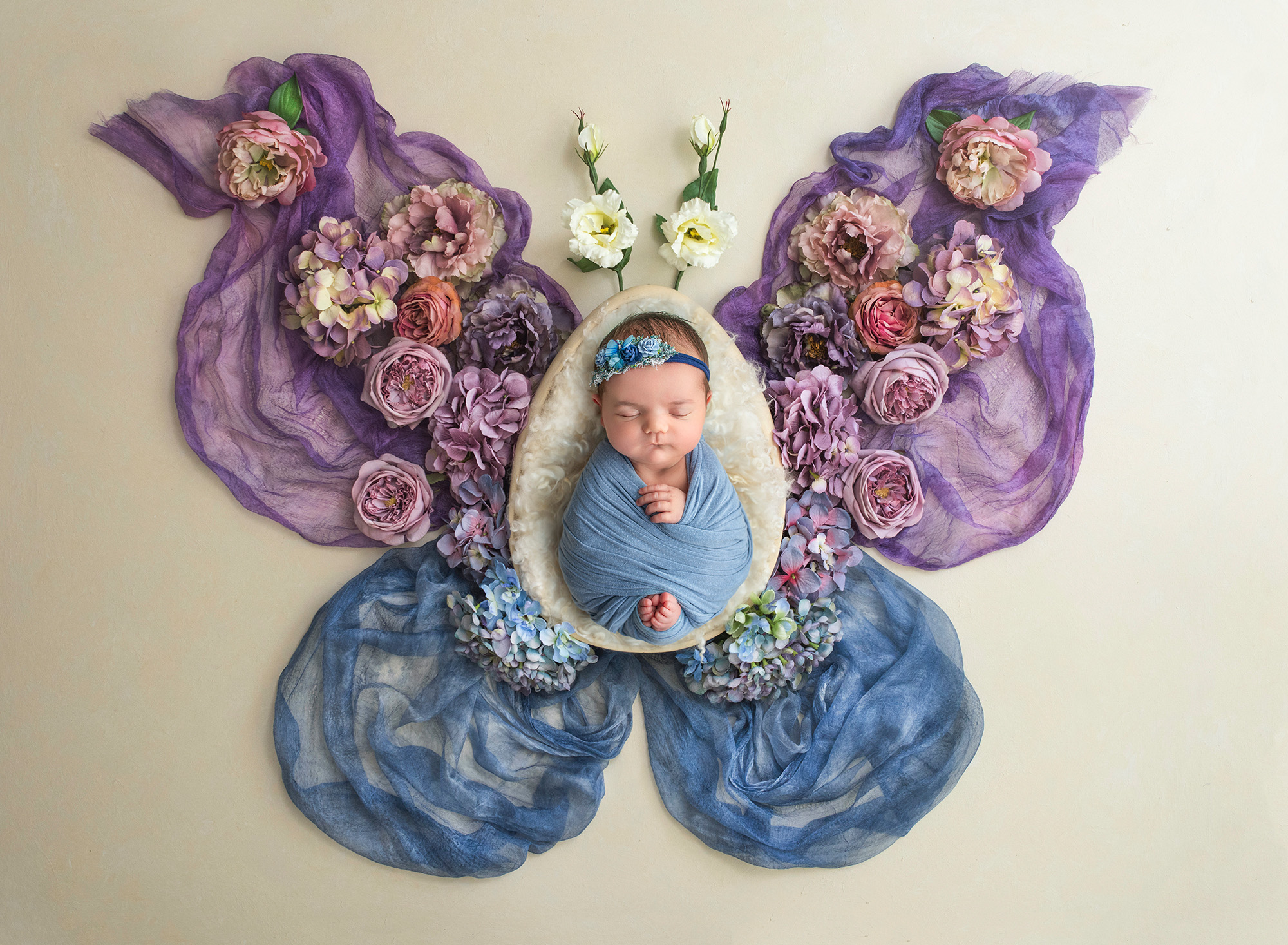 Newborn Studio Photography Newborn baby girl wrapped in blue lying inside a butterfly shape surrounded by delicate flowers