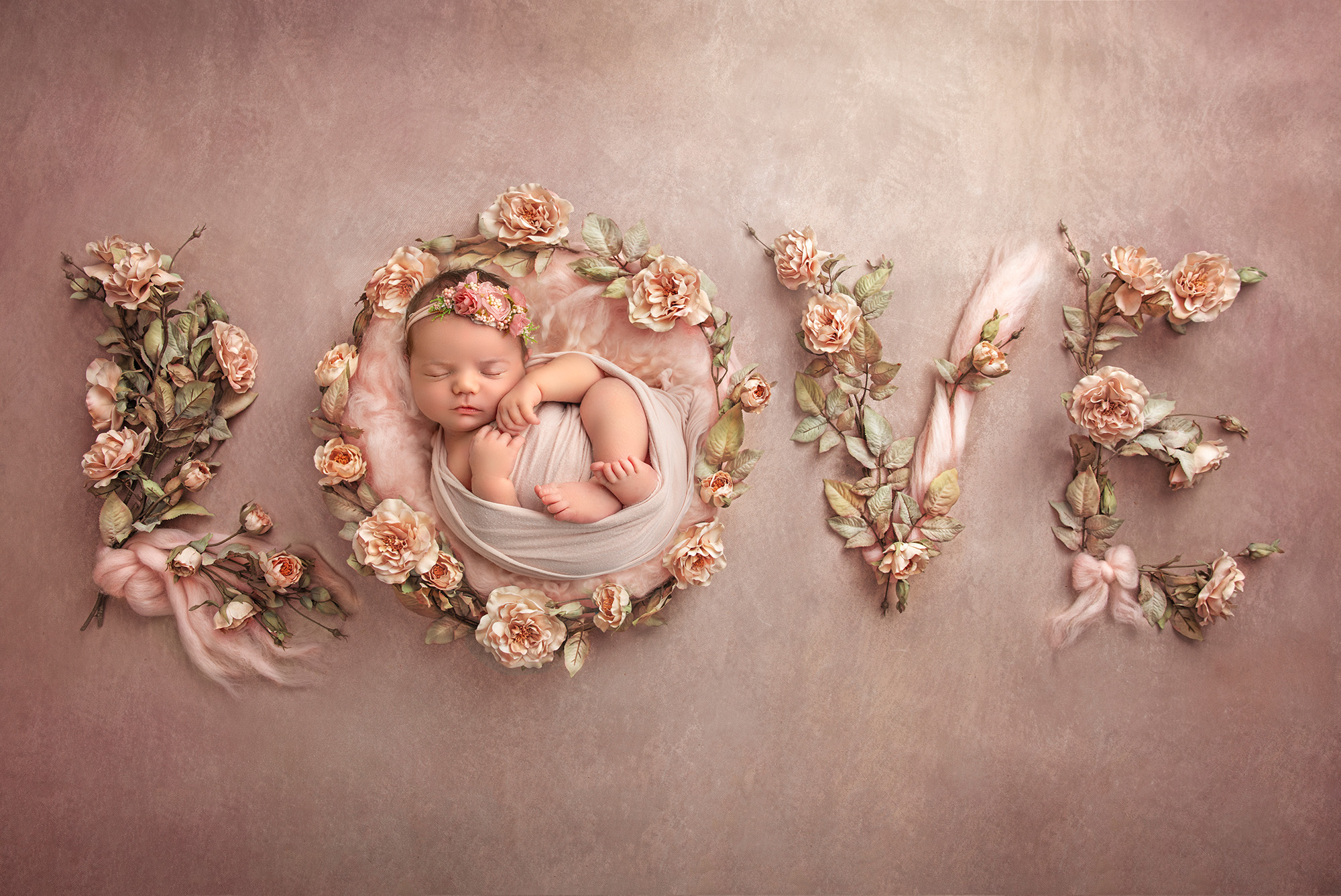 Newborn baby girl nestled inside the letter 'O', with the word "Love" spelled out on a pink background