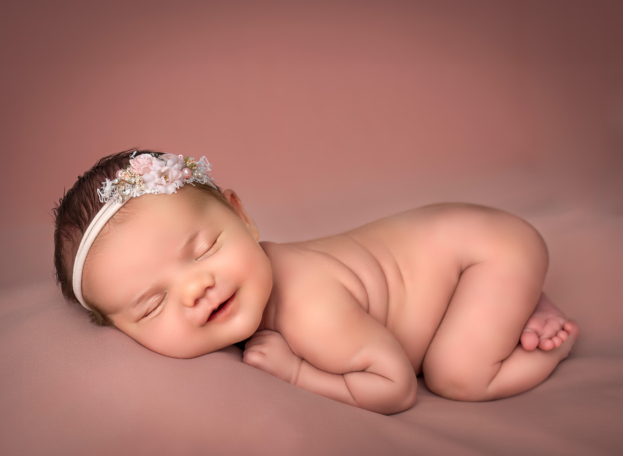 Newborn baby girl asleep naked on pink background displaying her back wrinkles