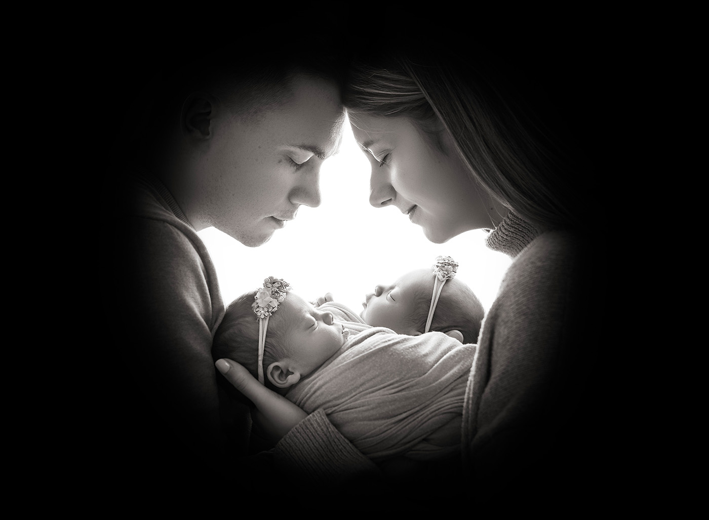 newborn twin photography mom and dad with heads together praying over their newborn twin girls in black and white photograph