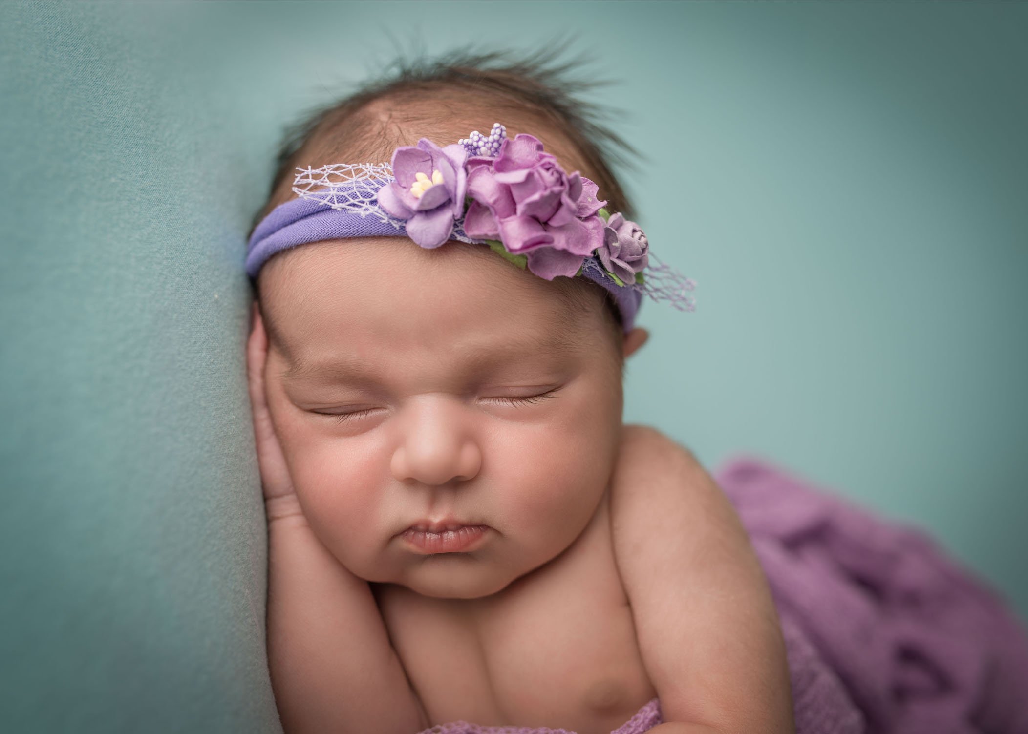 newborn girl on teal wearing purple floral headband
