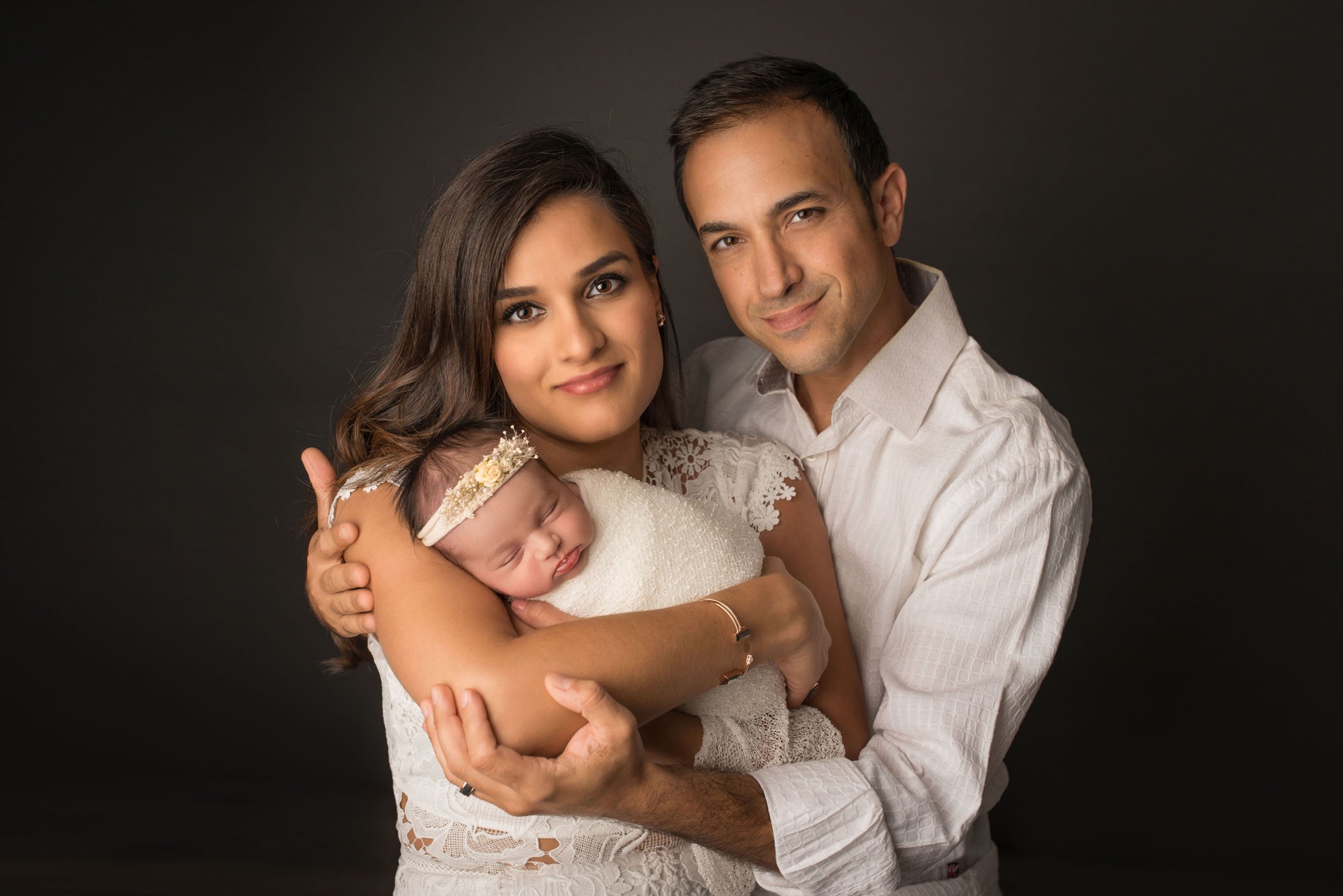 Mom holding newborn daughter with Dad wrapping arms around both
