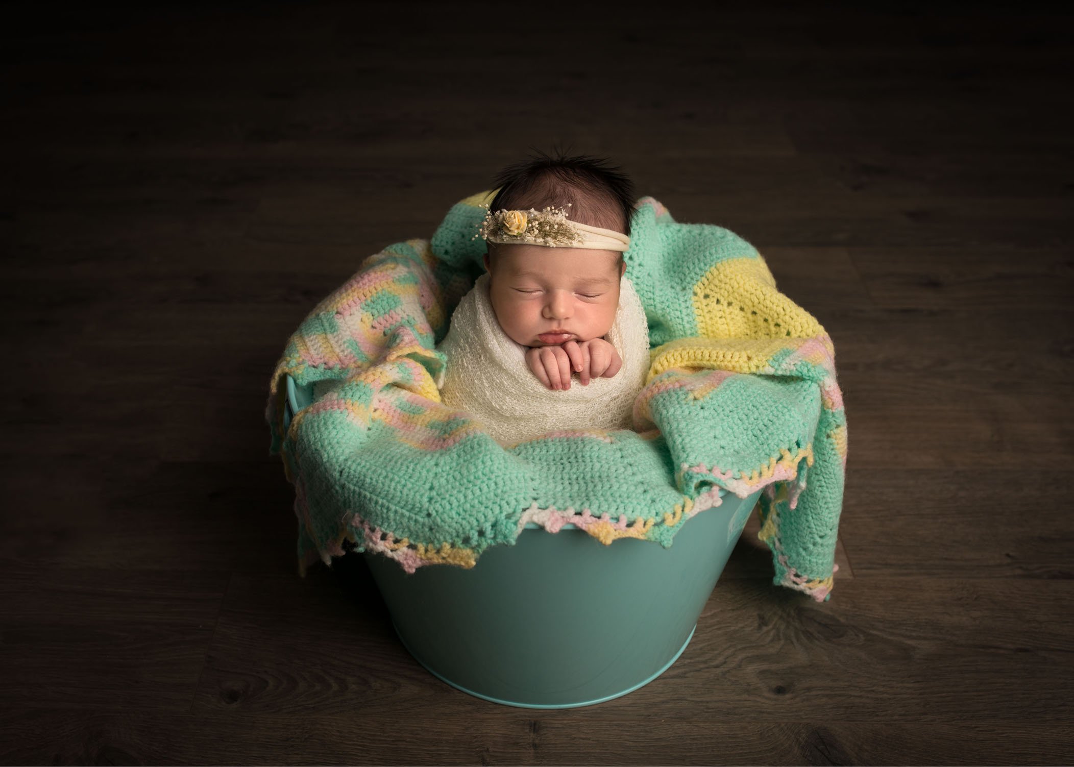 Newborn baby girl in teal bucket wrapped in antique crocheted quilt