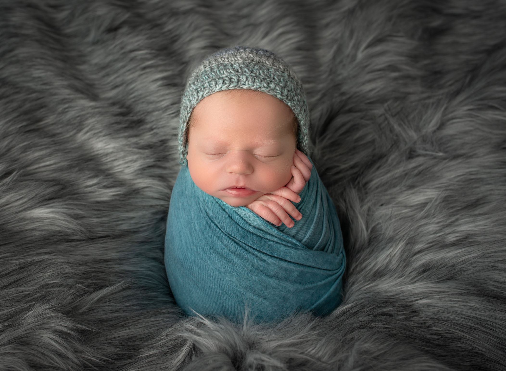Newborn baby swaddled in teal with matching bonnet in potato sack pose