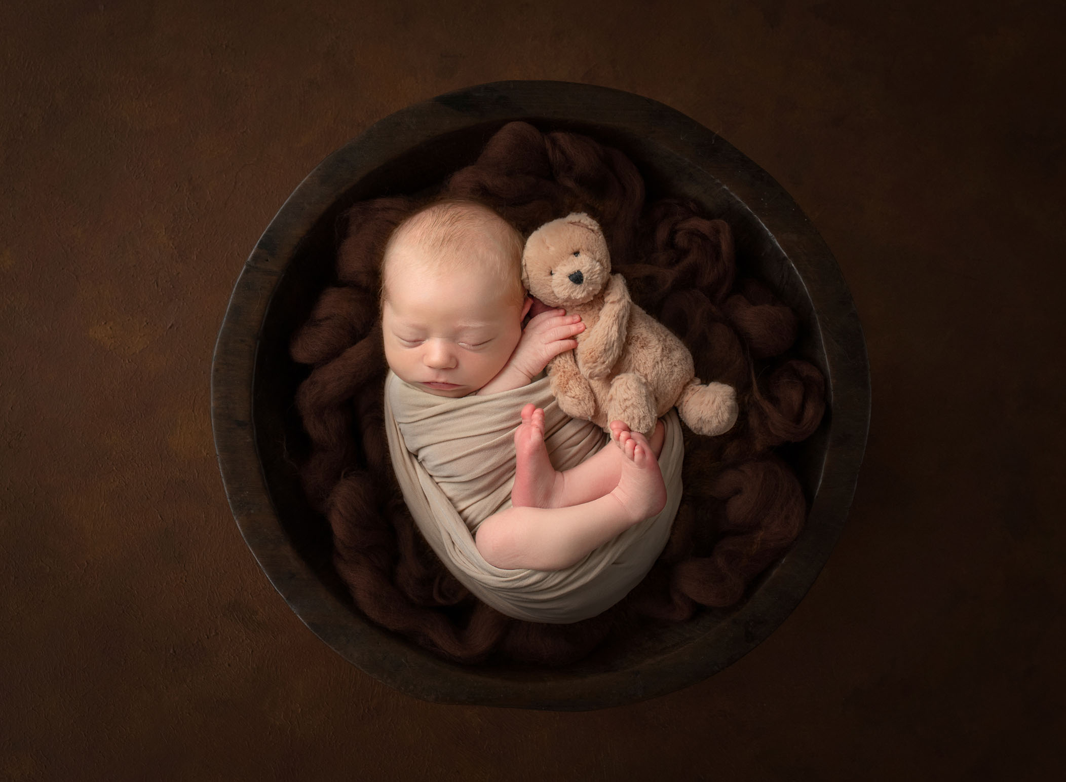Newborn baby and his teddy bear sleeping in a bowl swaddled