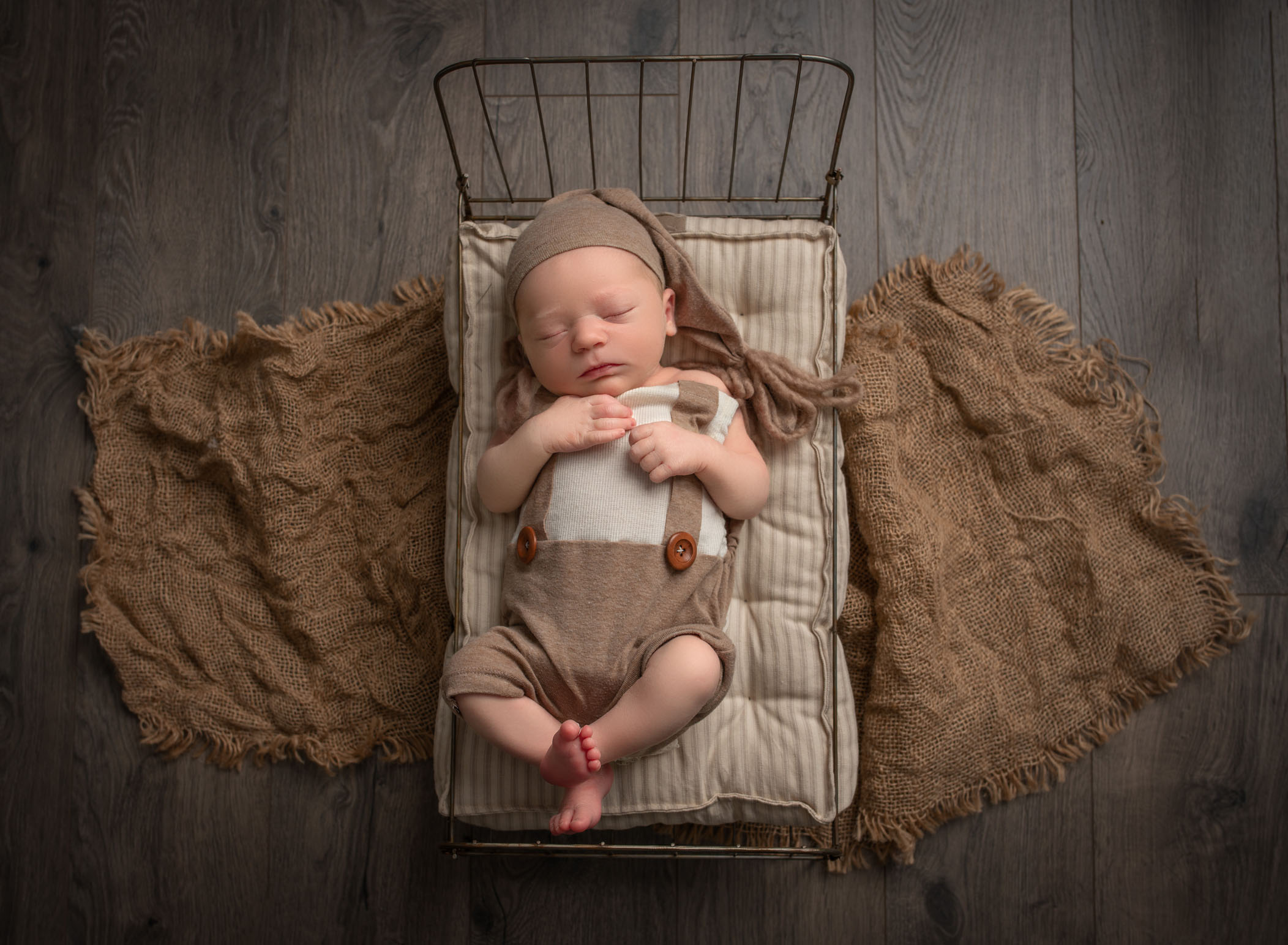 Newborn baby dressed in old fashioned suspenders and nite cap sleeping in wire framed bed