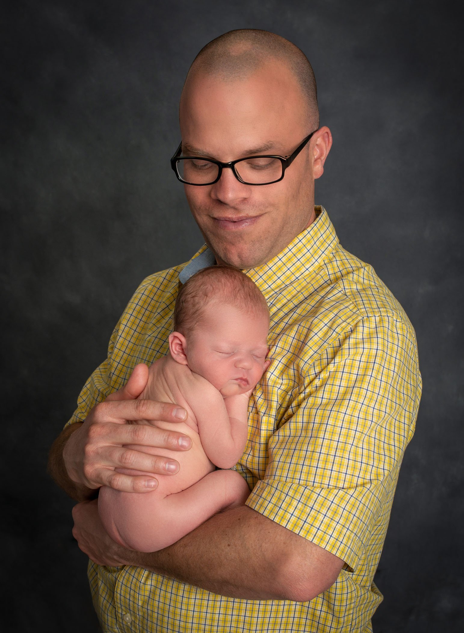 dad wearing glasses holds his newborn asleep on his chest