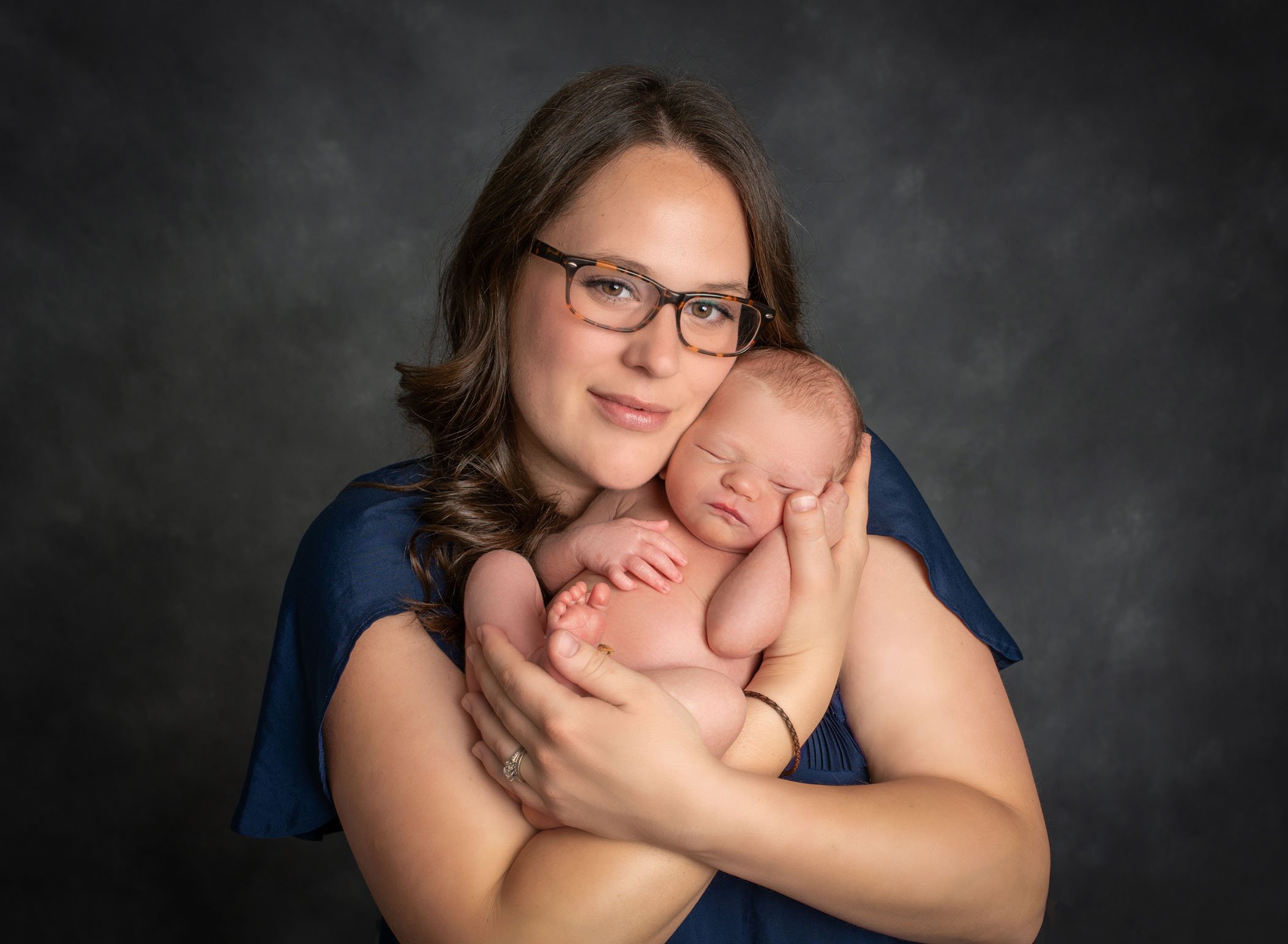 Mom wearing glasses holds her newborn in arms