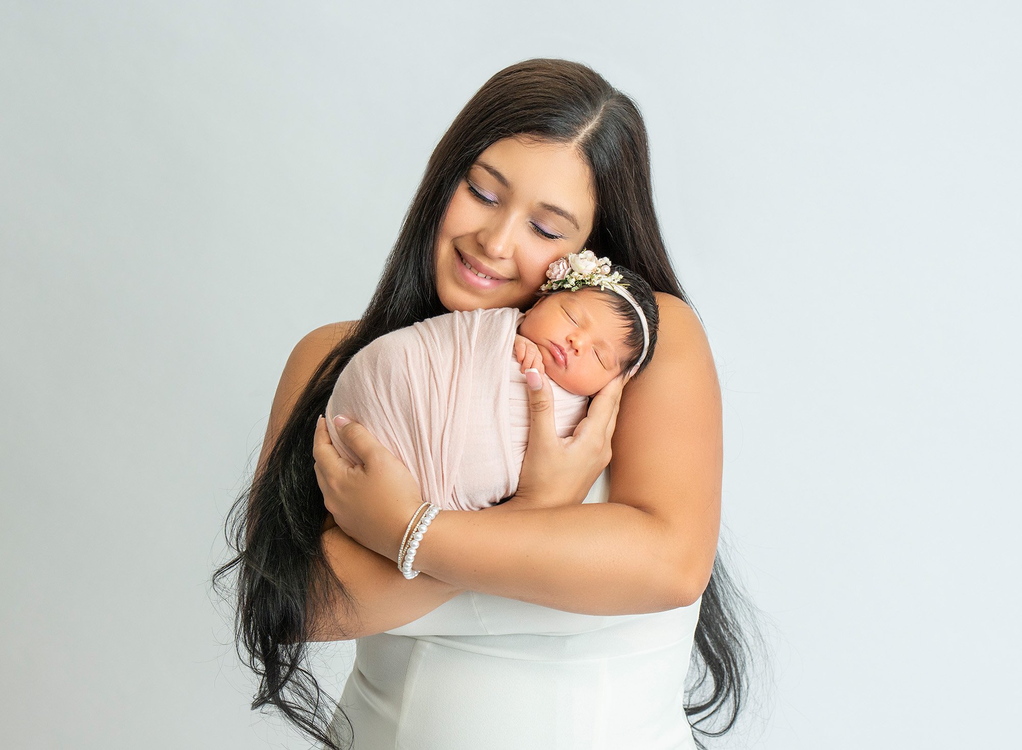 surrogate mom cradling newborn baby girl swaddled in light pink