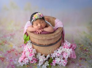 newborn baby girl asleep inside of honey pot surrounded by pink and white flowers