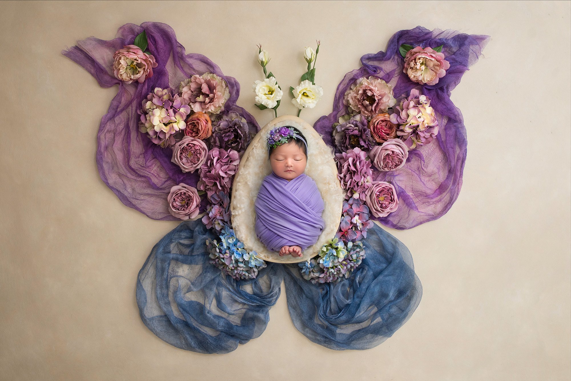 sweet newborn baby girl asleep swaddled in purple inside of a butterfly