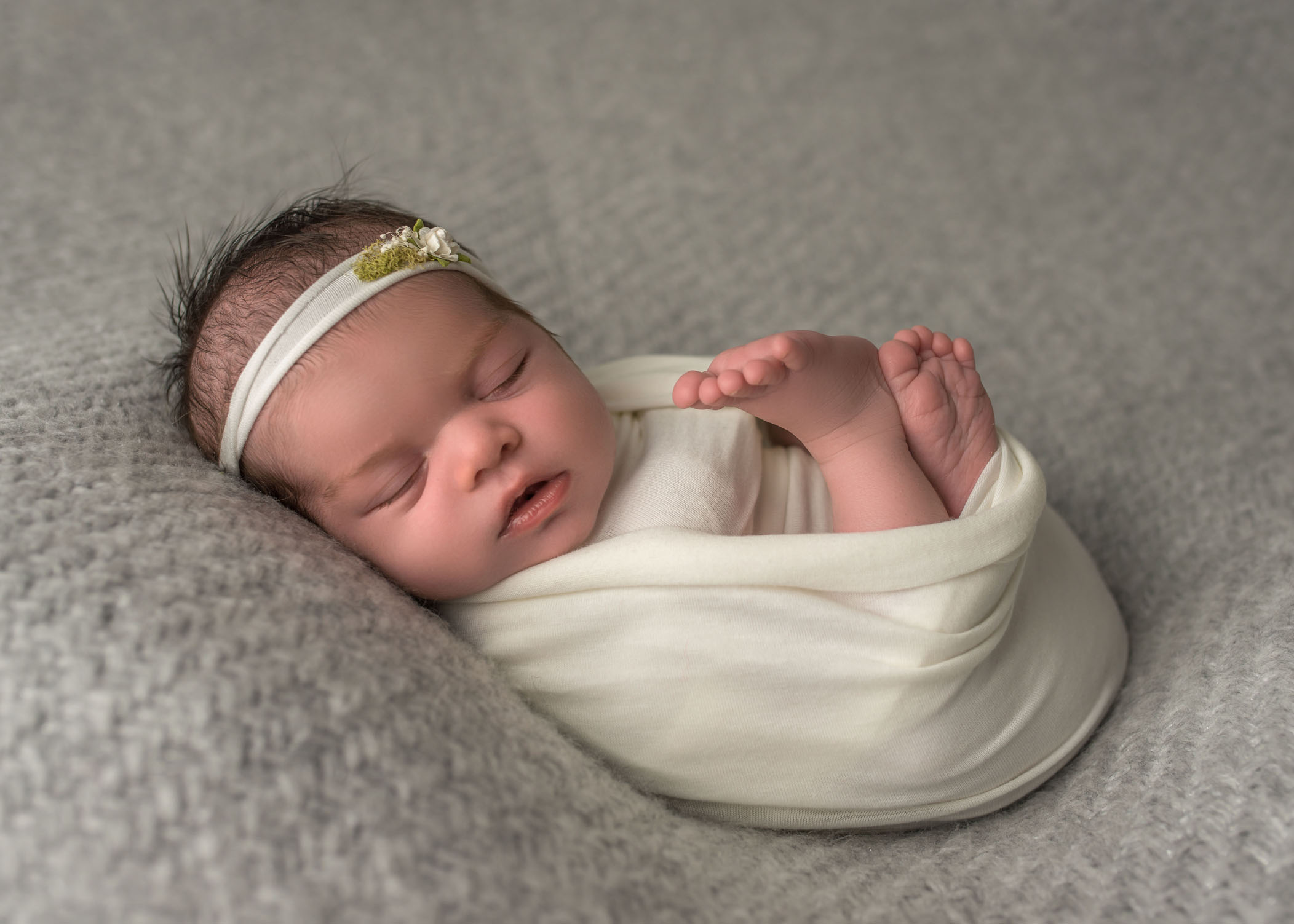 newborn baby girl sleeping on grey blanket with feet sticking out of swaddle