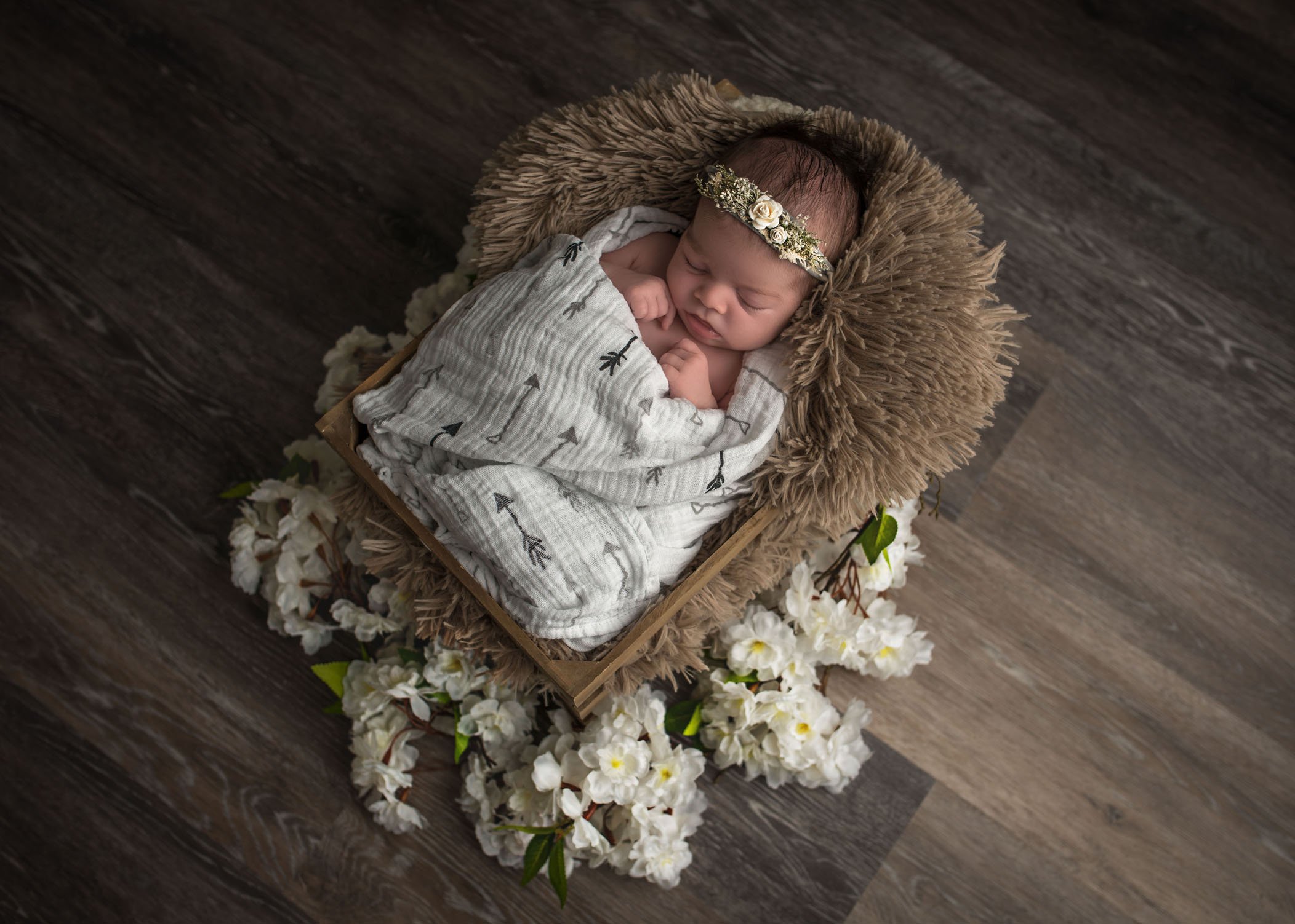 newborn baby girl sleeping in crate with flowers and headband
