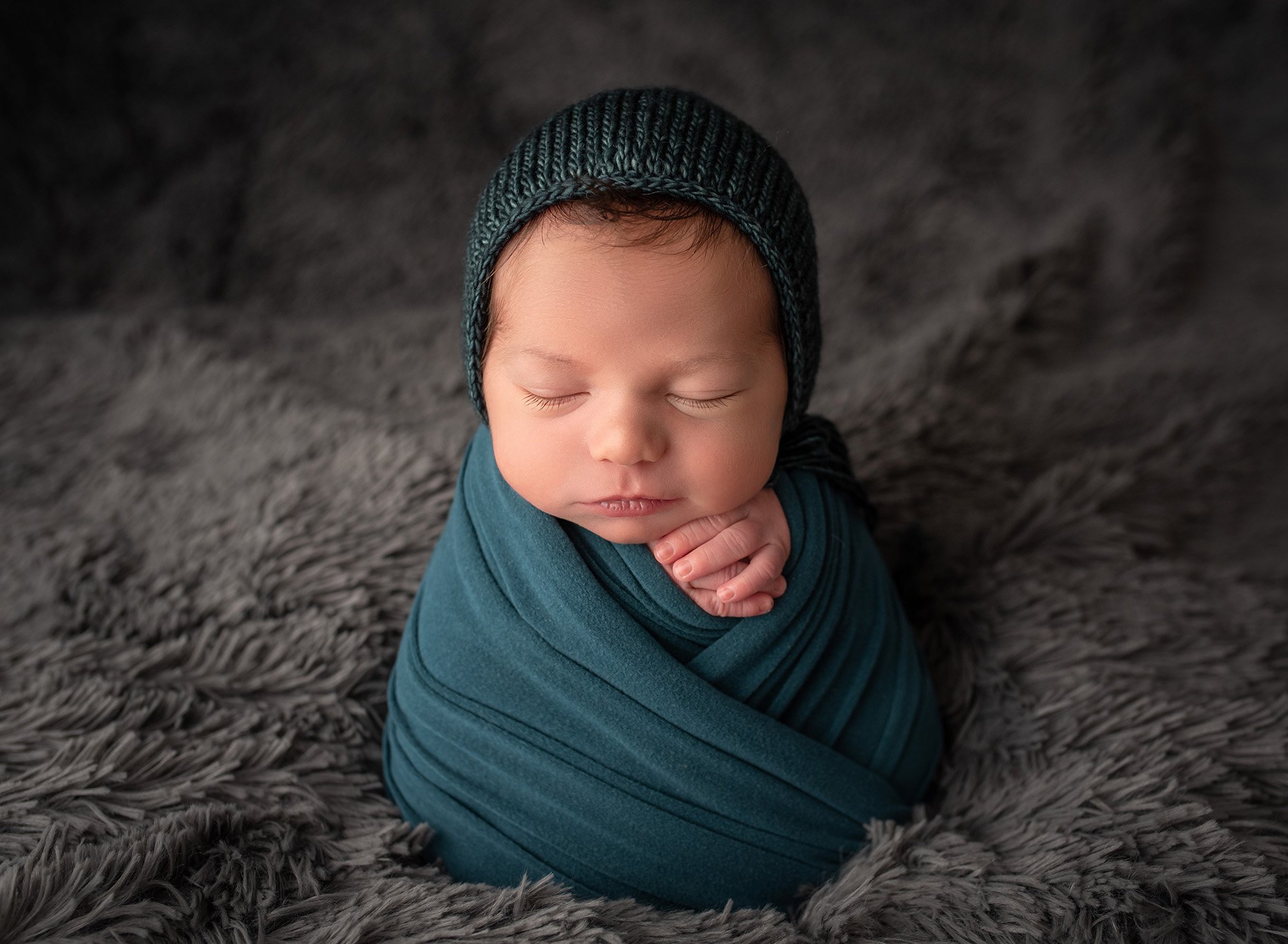 asleep newborn baby boy swaddled in dark teal wearing bonnet