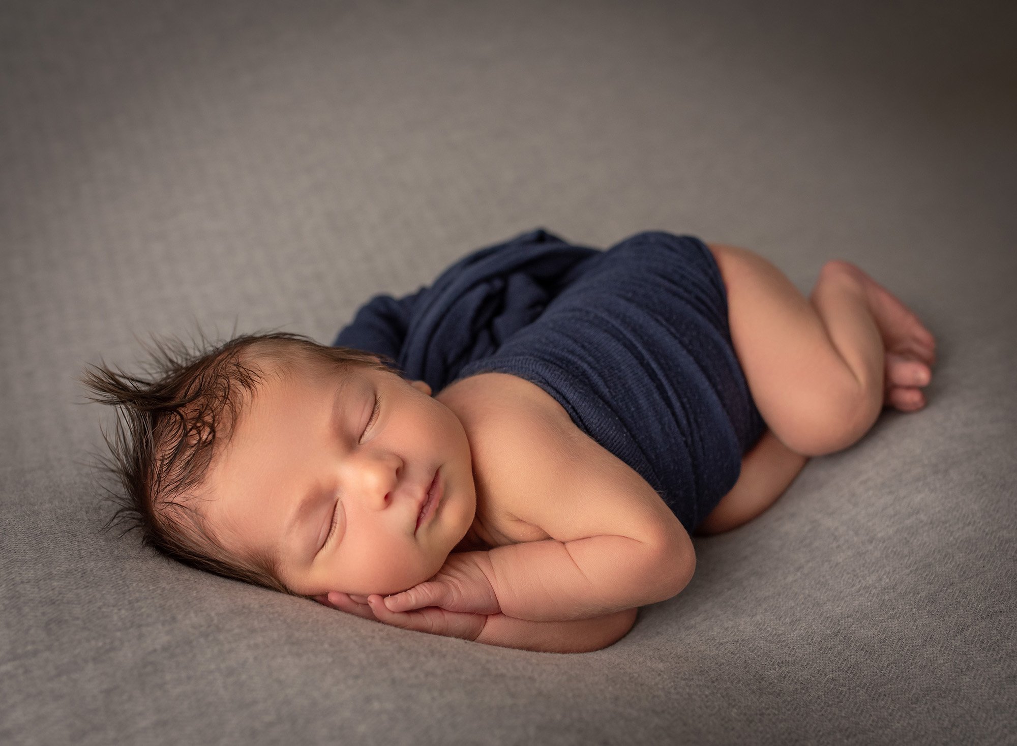 newborn baby boy asleep on his side wearing blue wrap 