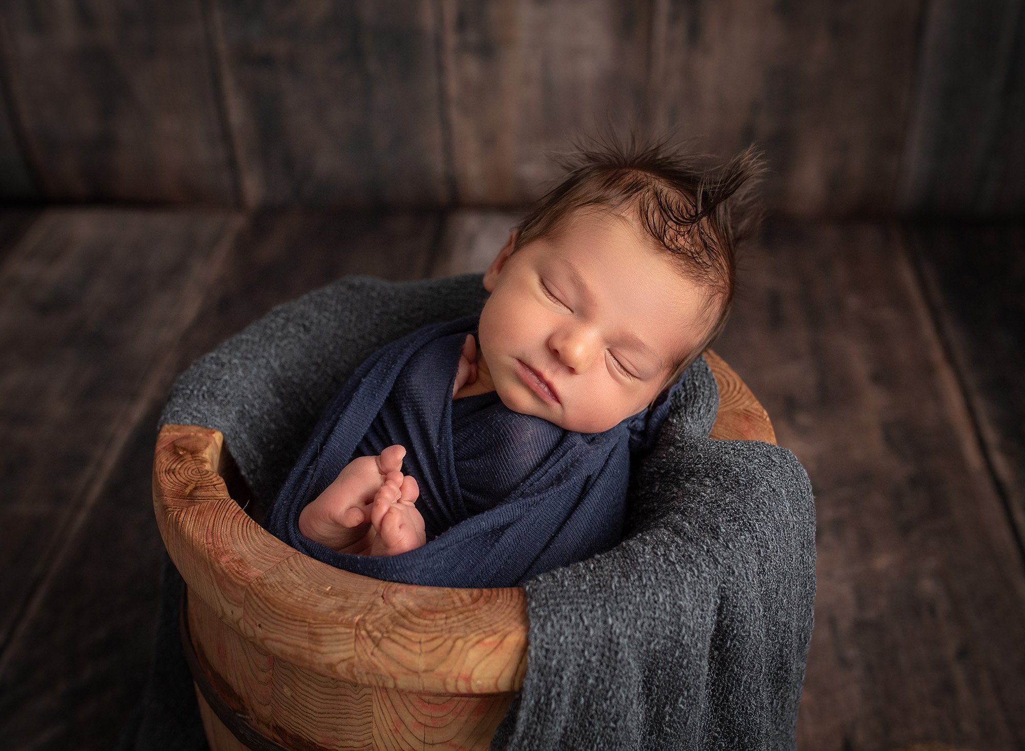newborn baby boy swaddled in blue asleep in wooden pot