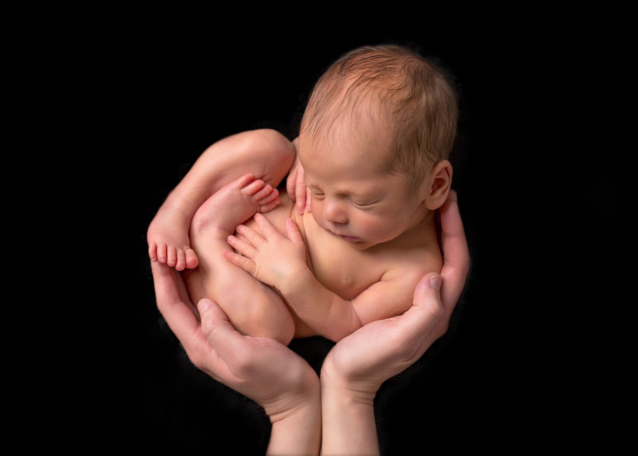 newborn boy cradled in his mom's hands on black background