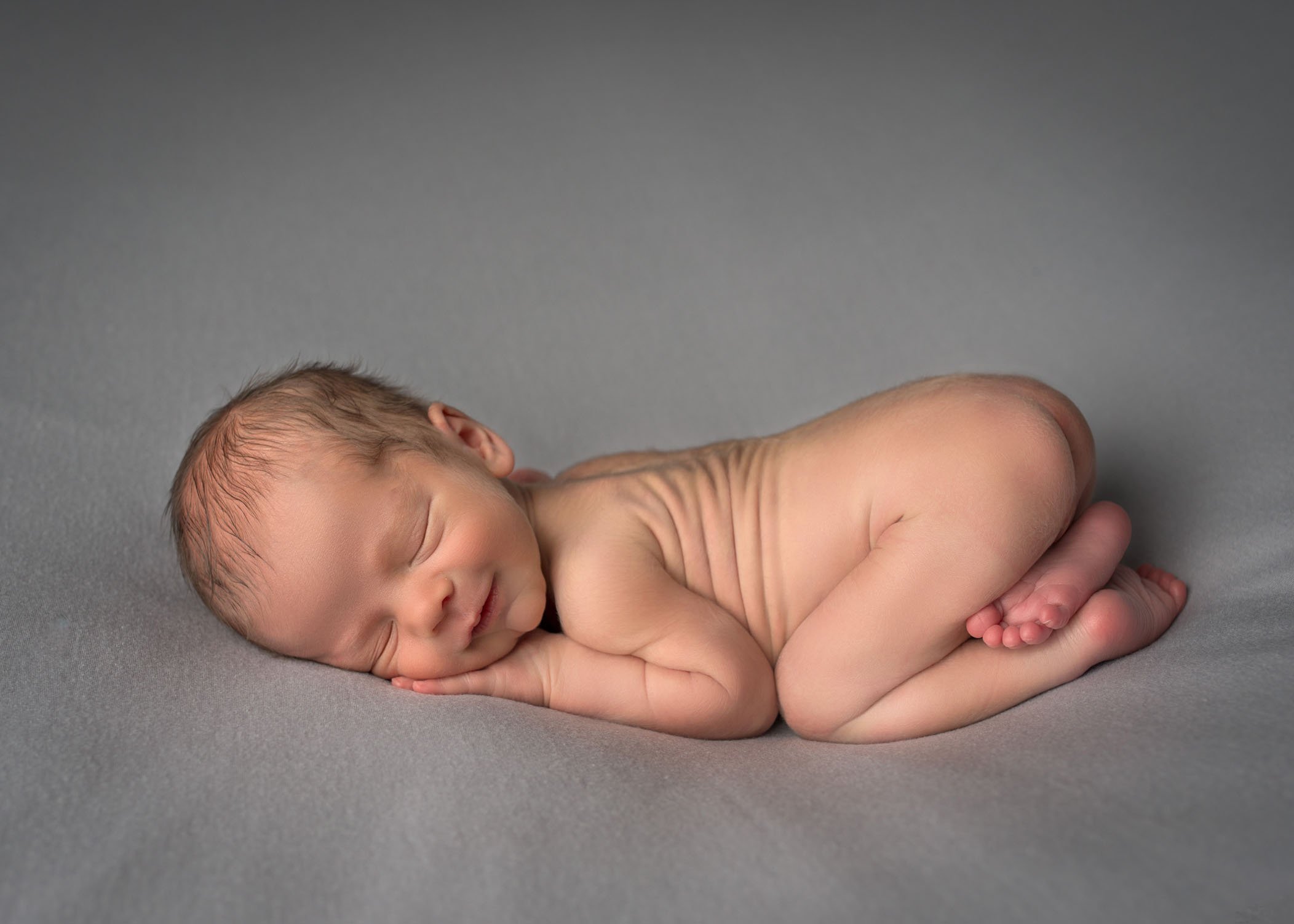 newborn boy sleeping in bum up pose on grey background smiling