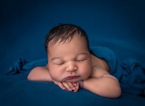 newborn baby boy asleep with his head on his hands in a blue blanket