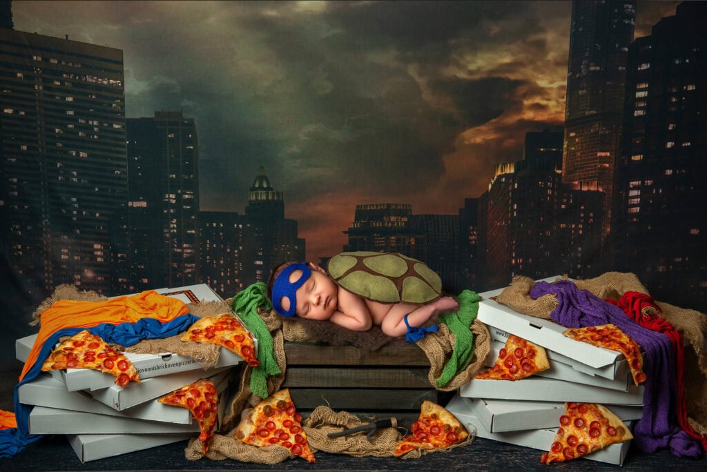 best newborn photographer dressed the baby up as a ninja turtle sleeping on boxes of pizza in a city scape