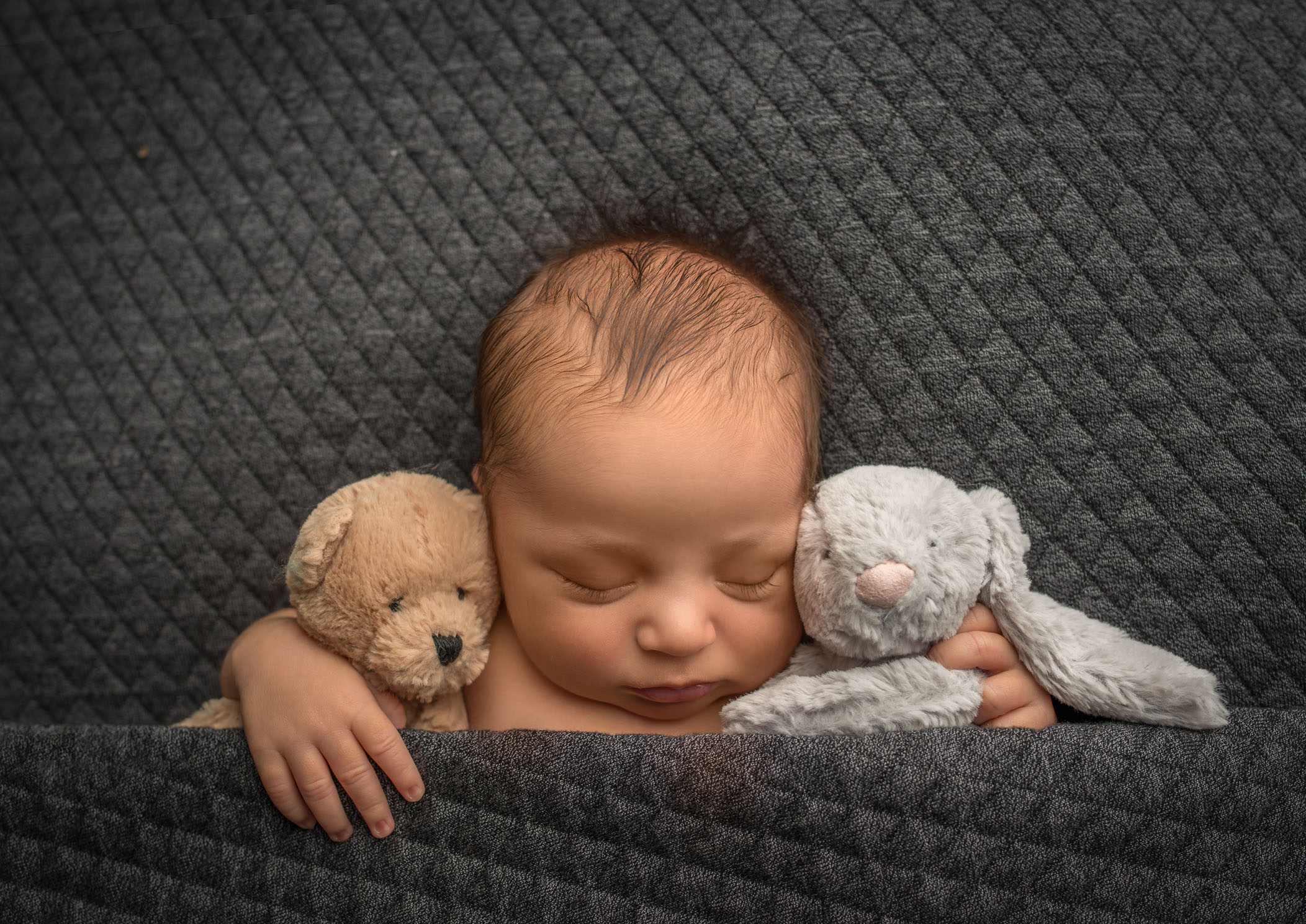 newborn baby sleeping tucked in with stuffed bear and rabbit
