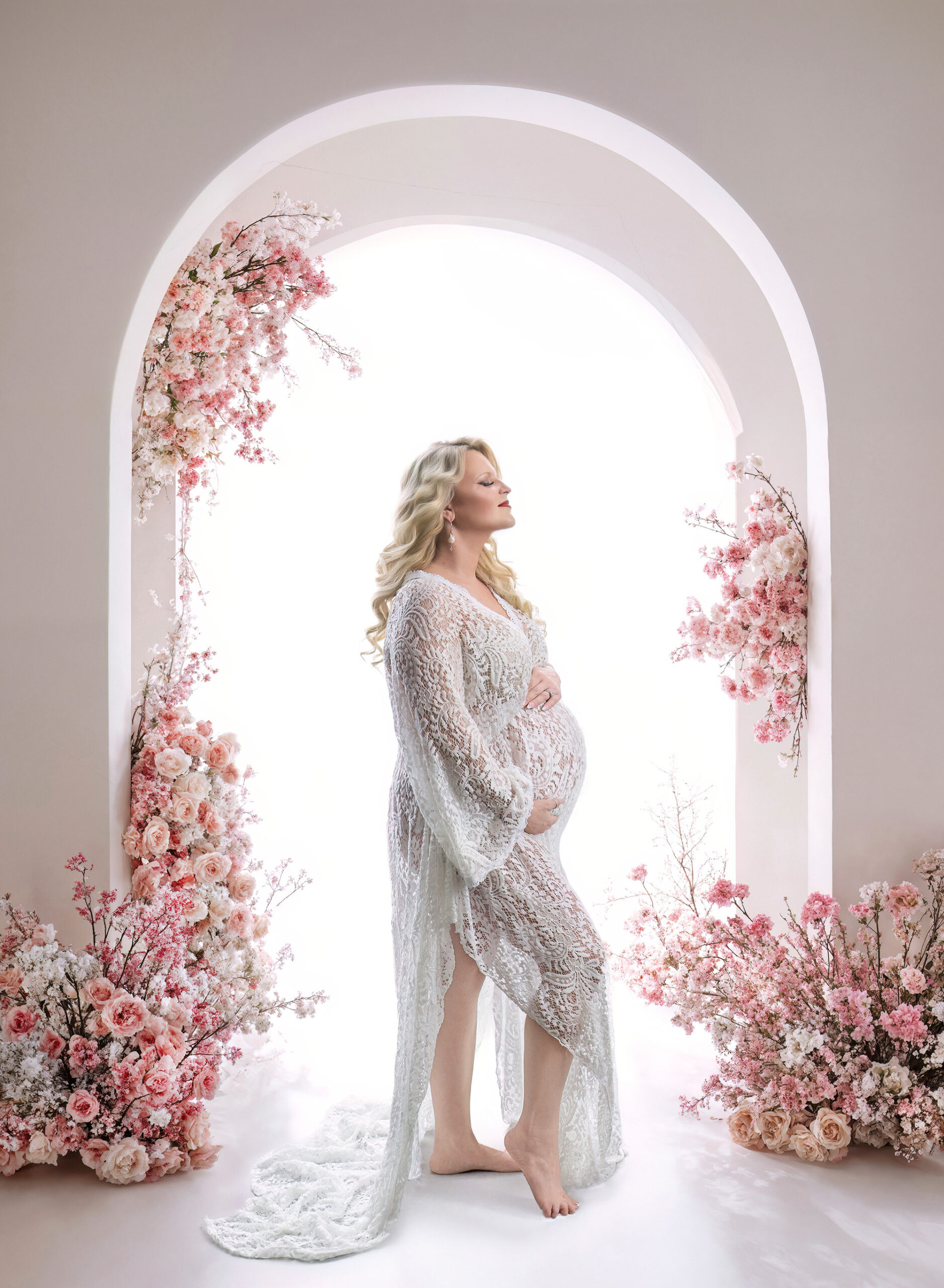 pregnant mom backlit in front of white archway covered in pink roses