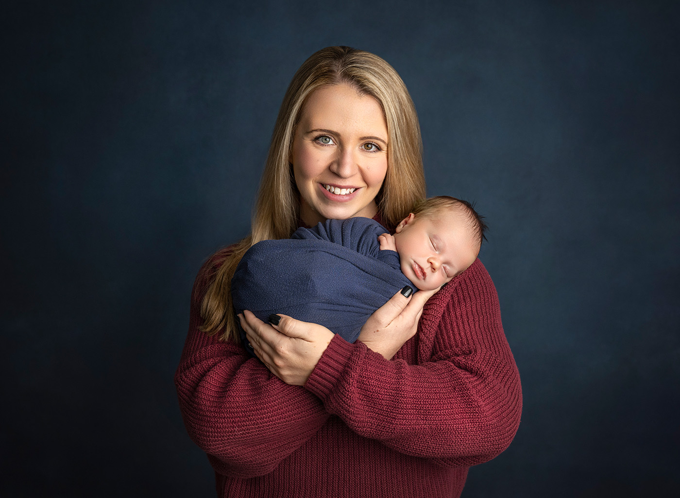 newborn boy photos mom holding her newborn son in both of her hands smiling at the camera
