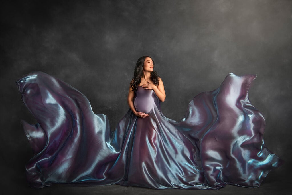 Luxury Maternity Photographer pregnant woman draped in blue and purple irridecent silk that is flowing around her