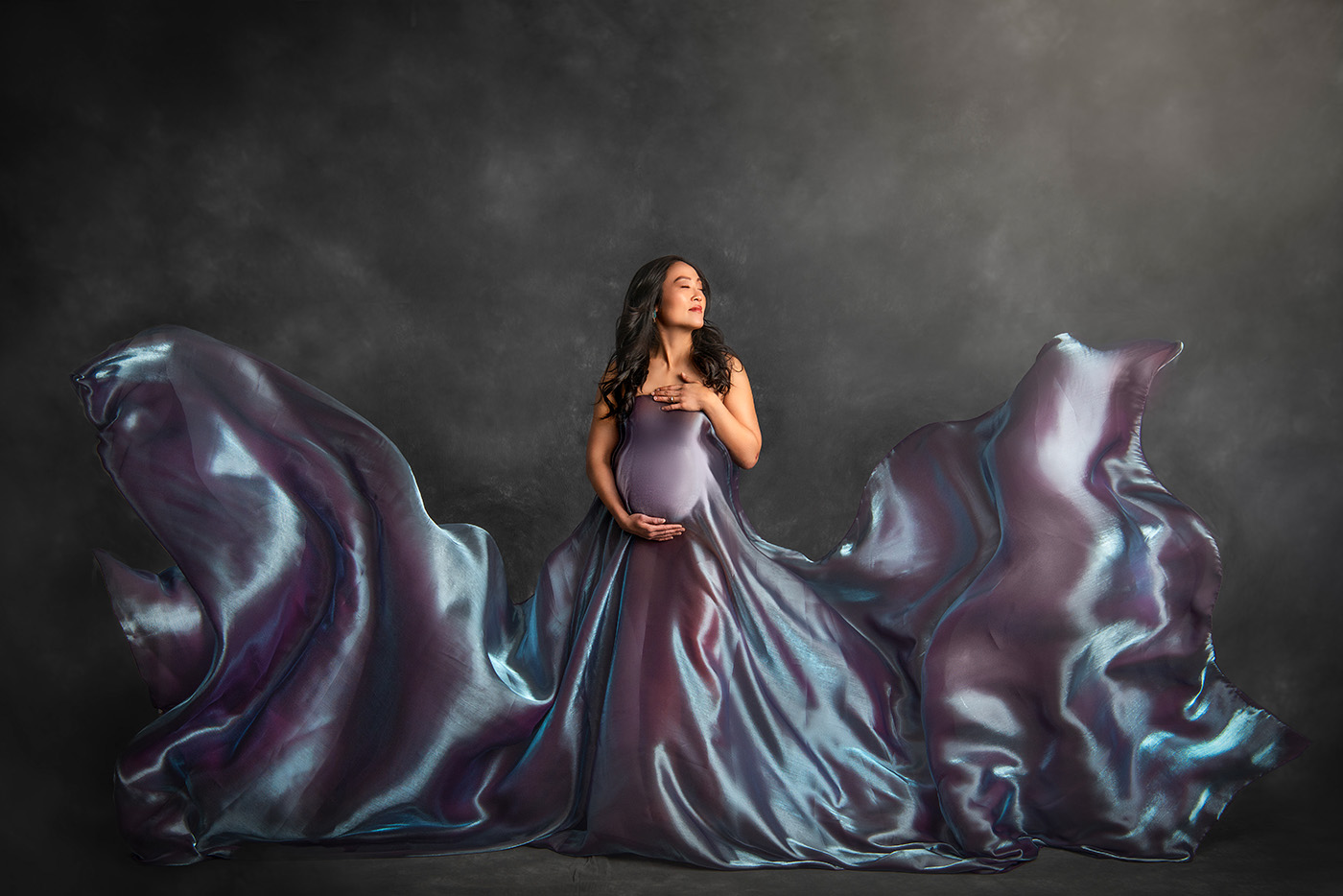 Luxury Maternity Photography pregnant woman draped in blue and purple irridecent silk that is flowing around her 