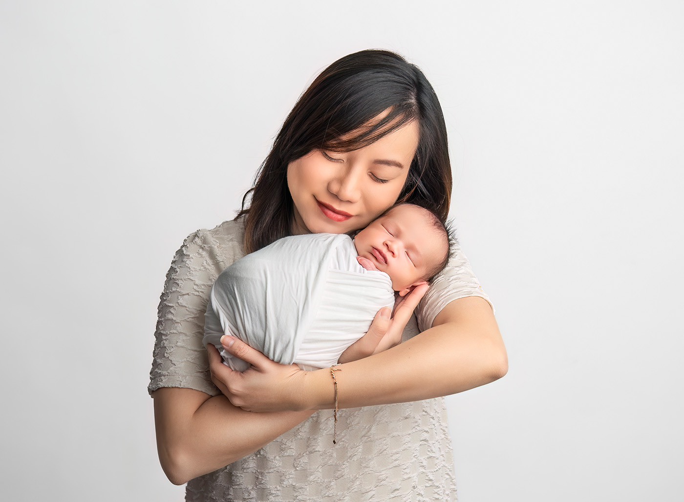 vietnamese mom holding her newborn baby close to her cheek and smiling