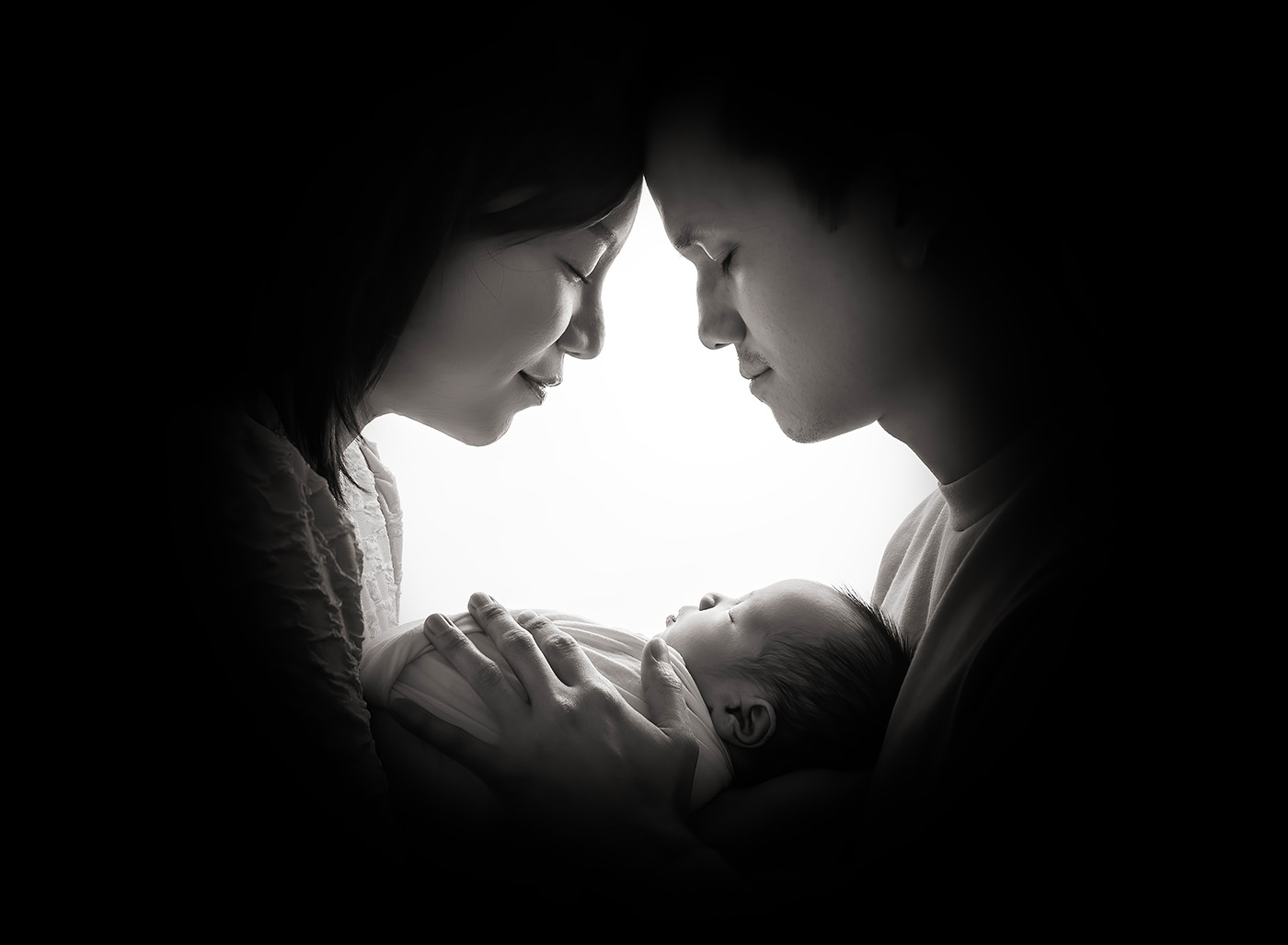 newborn parents watching over their new baby with heads together in black and white