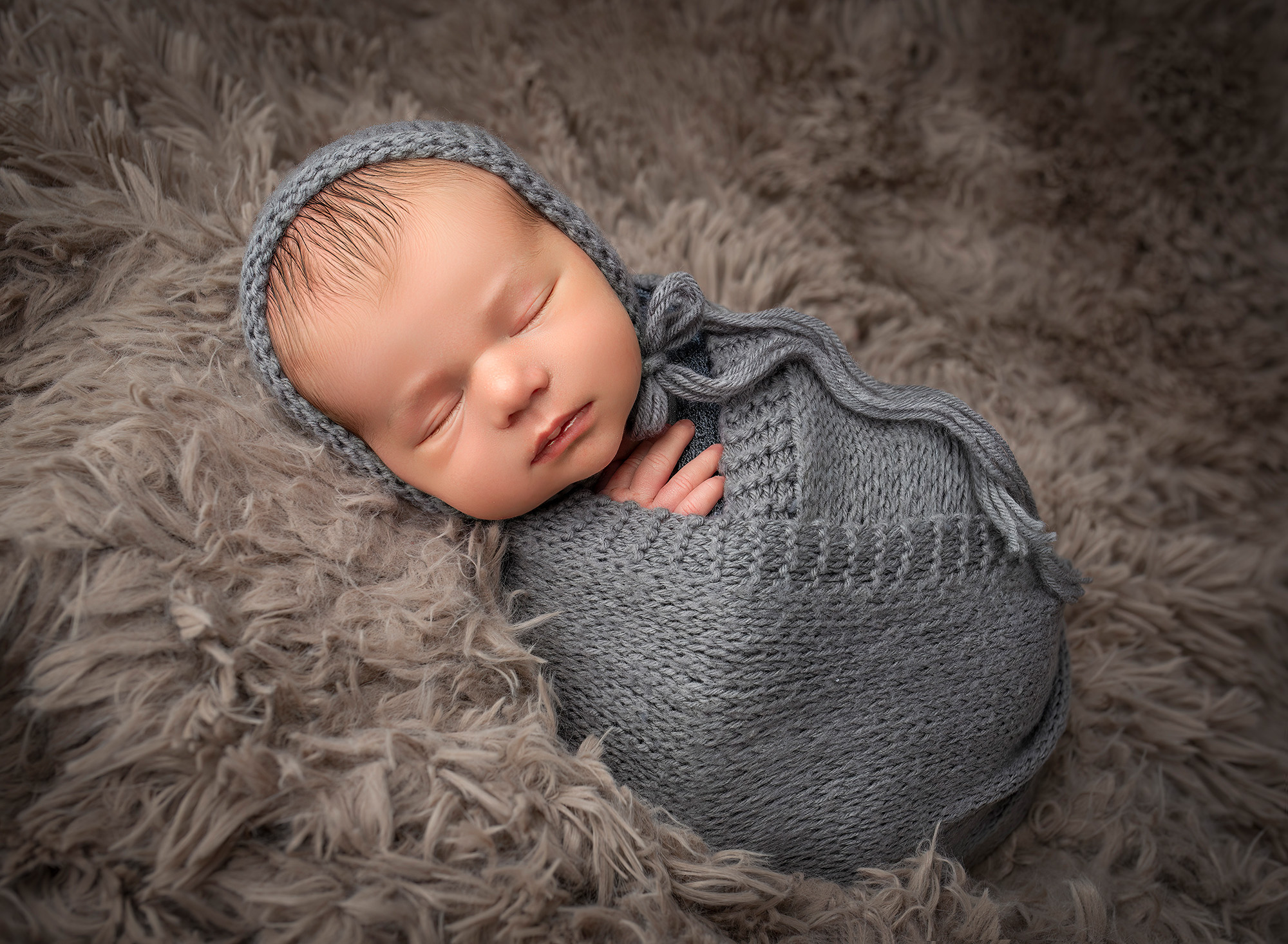 newborn boy sleeping on his side wearing a grey bonnet and grey knit wrap