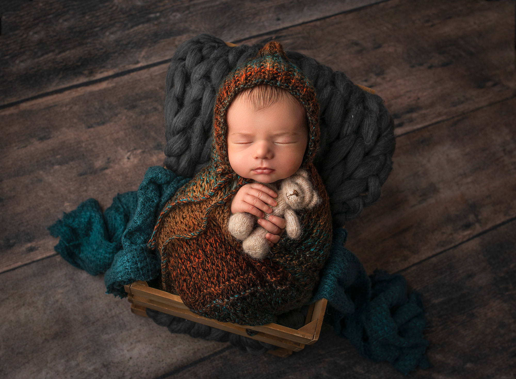 newborn baby boy sleeping in a crate holding a teddy bear