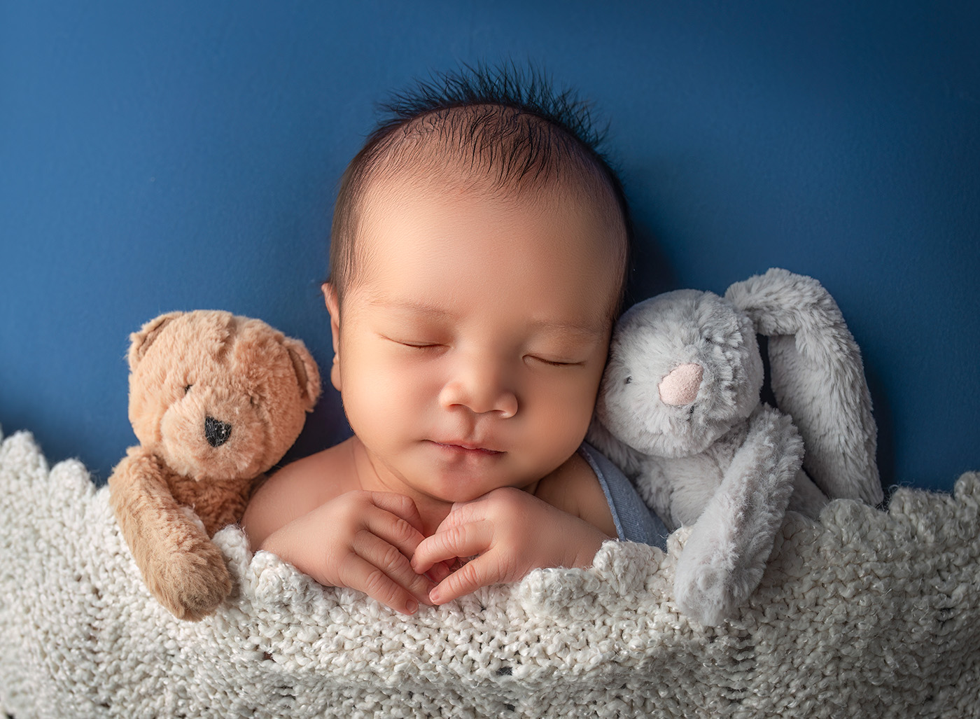 newborn baby boy sleeping tucked in with a teddy bear and a bunny rabbit