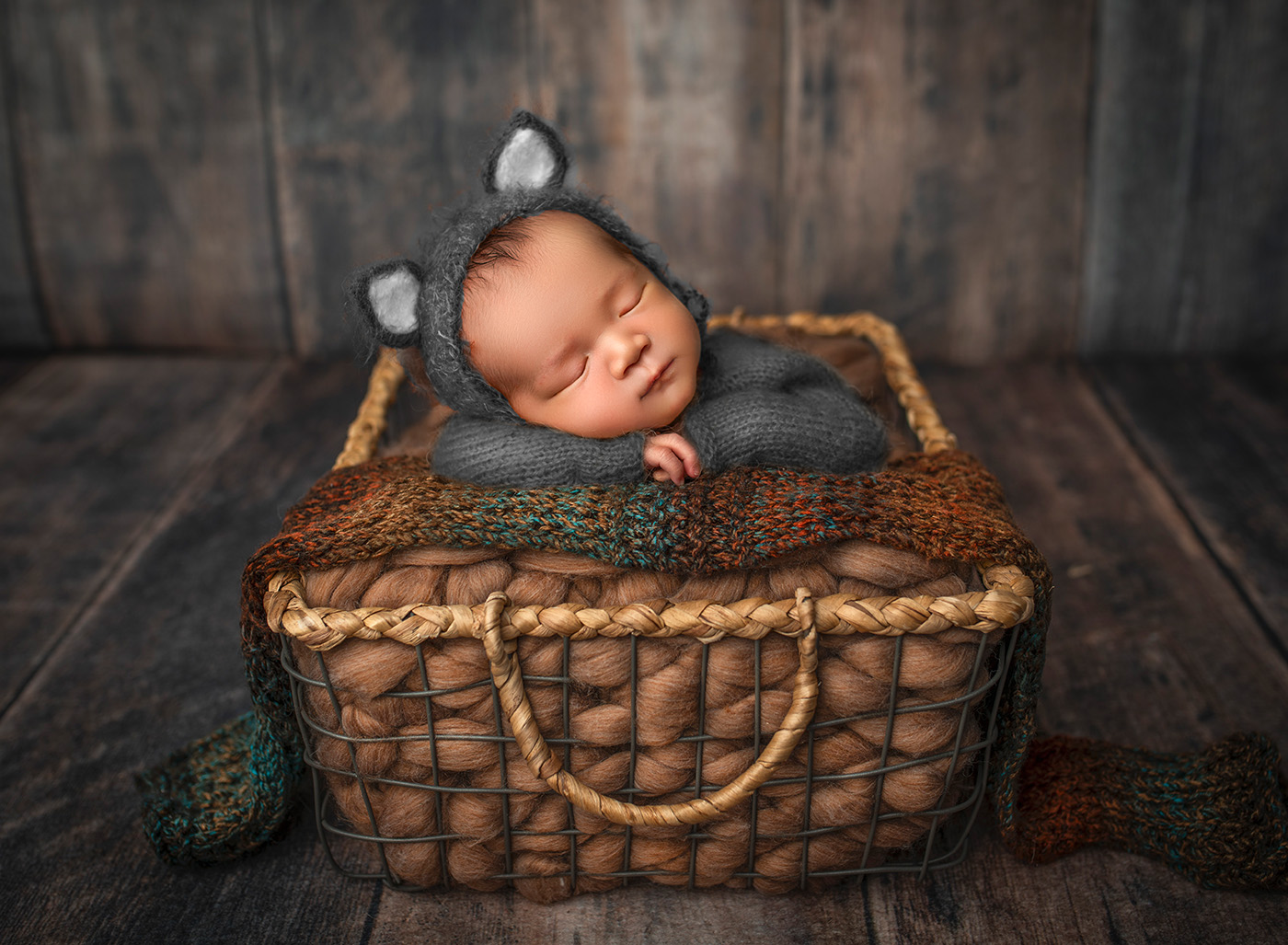 newborn baby dressed as a grey kitty cat sleeping in a basket with his head on his hands