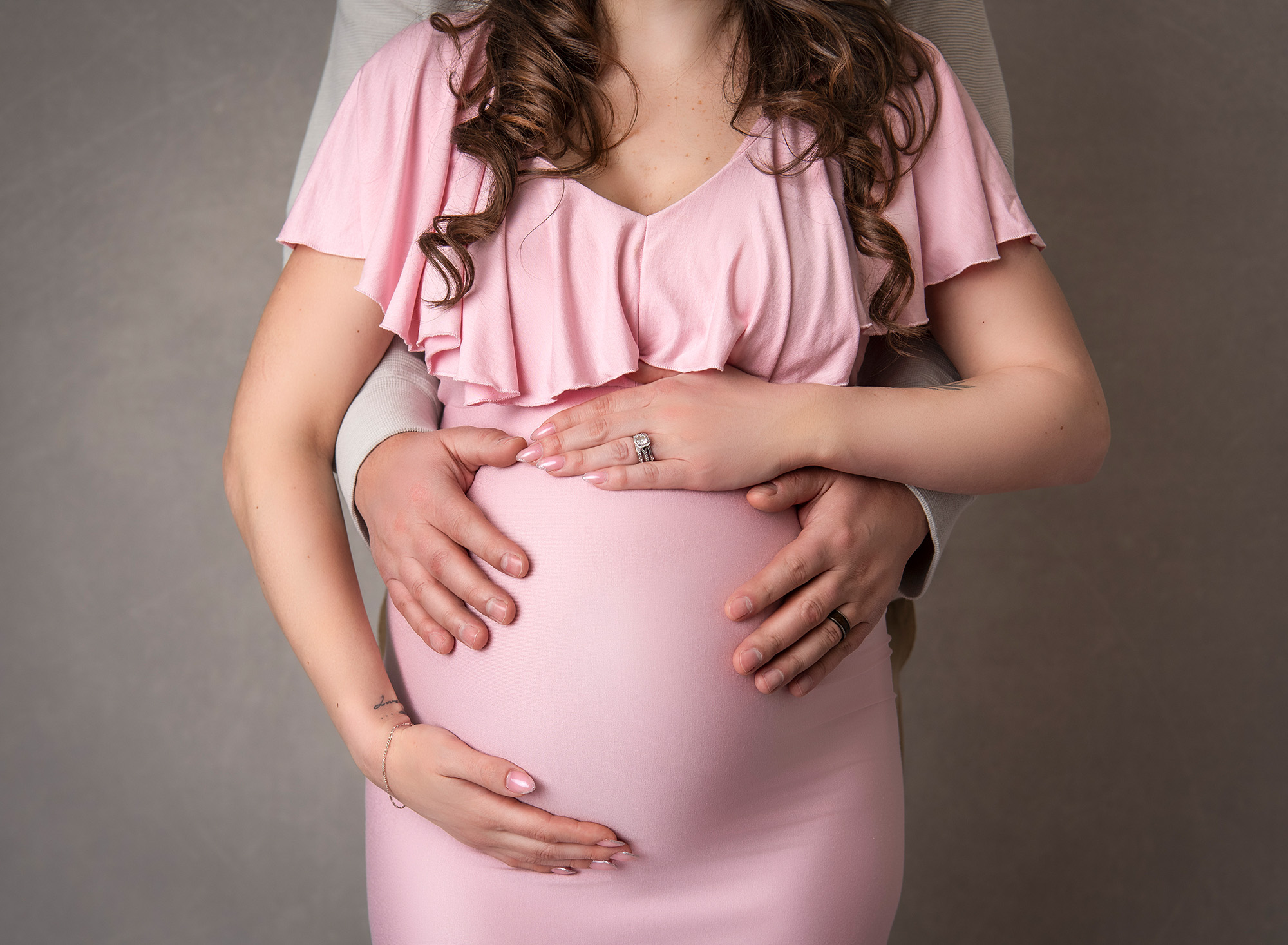woman wearing baby pink maternity dress cradling growing belly with her and dads hands