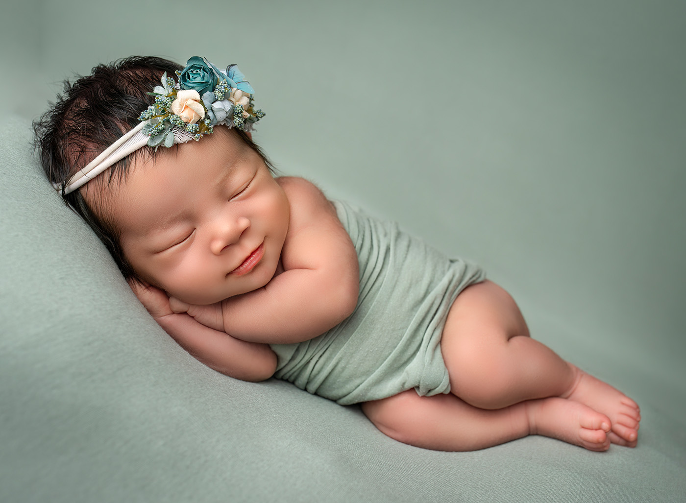 Luxury Newborn Photographer baby sleeping on her side and smiling on green background