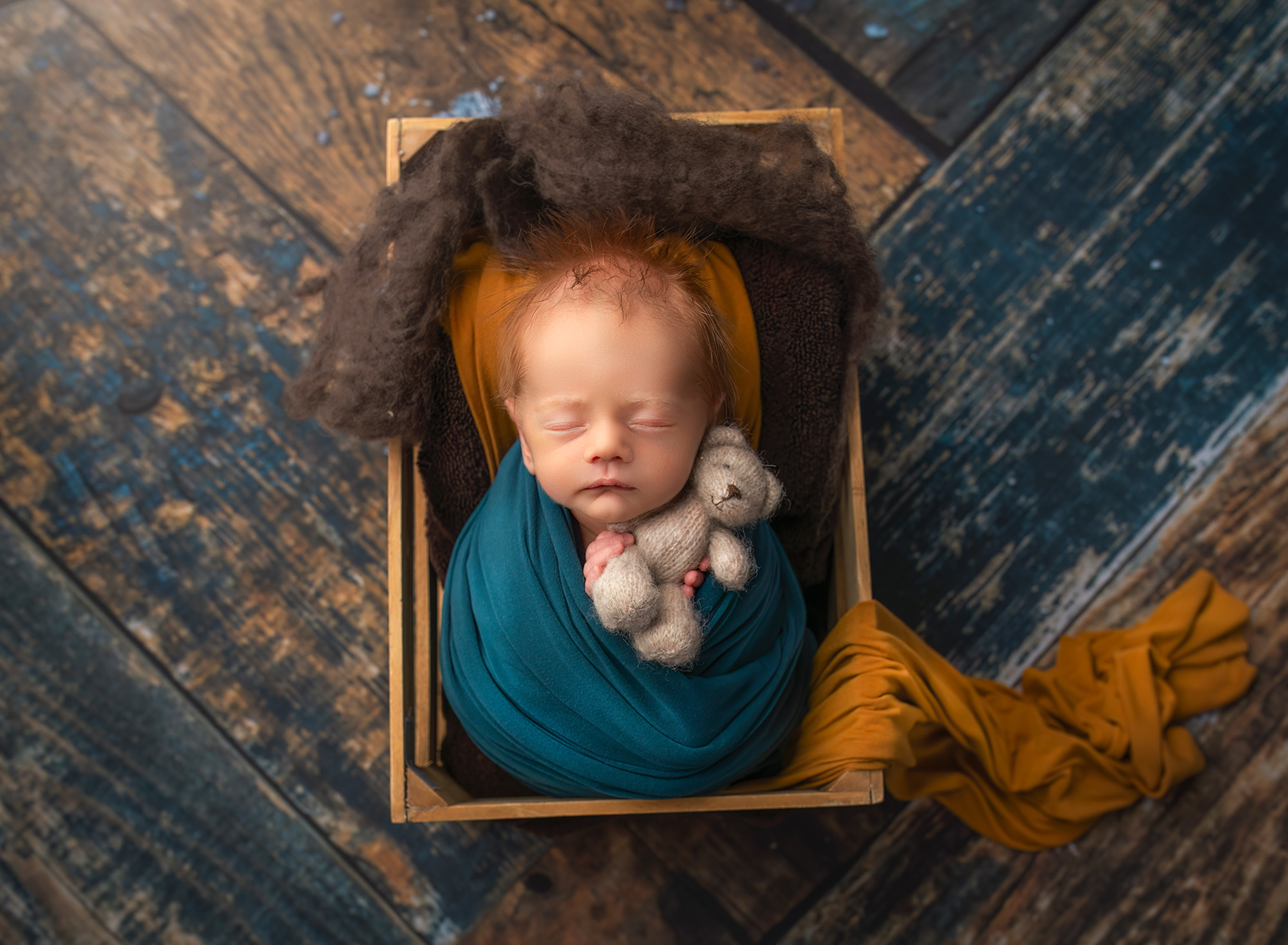 newborn baby boy wrapped in teal asleep in a crate holding a teddy bear